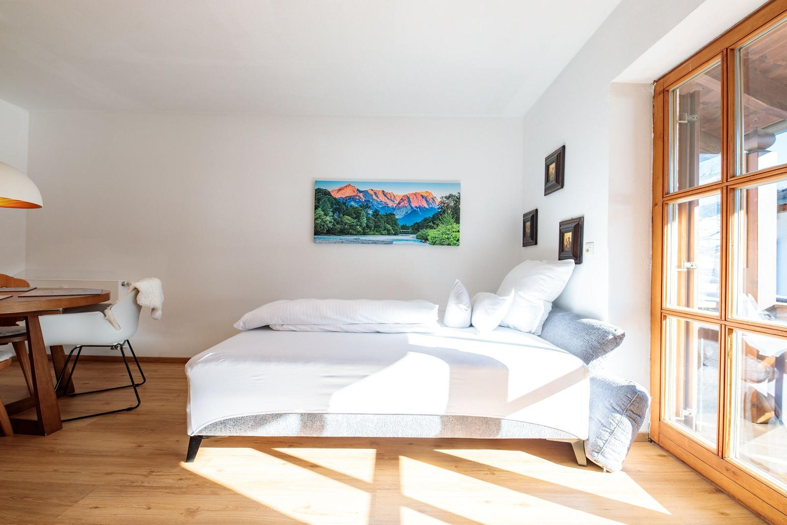 Schlafzimmer mit Bett, Tisch und Wandbild. Holzfenster und helles Holzfußboden.
