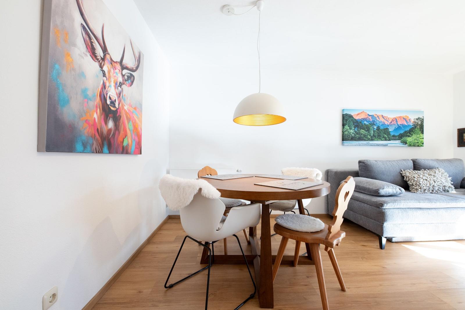 Esszimmer mit Tisch, Stühlen und Wandbildern. Sofa im Hintergrund.
