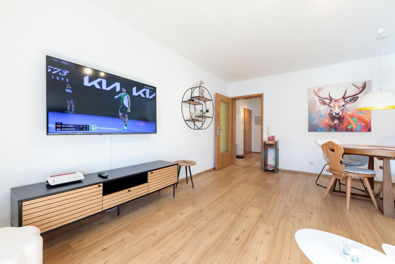 Wohnbereich mit Fernseher, Esstisch und Wandbild