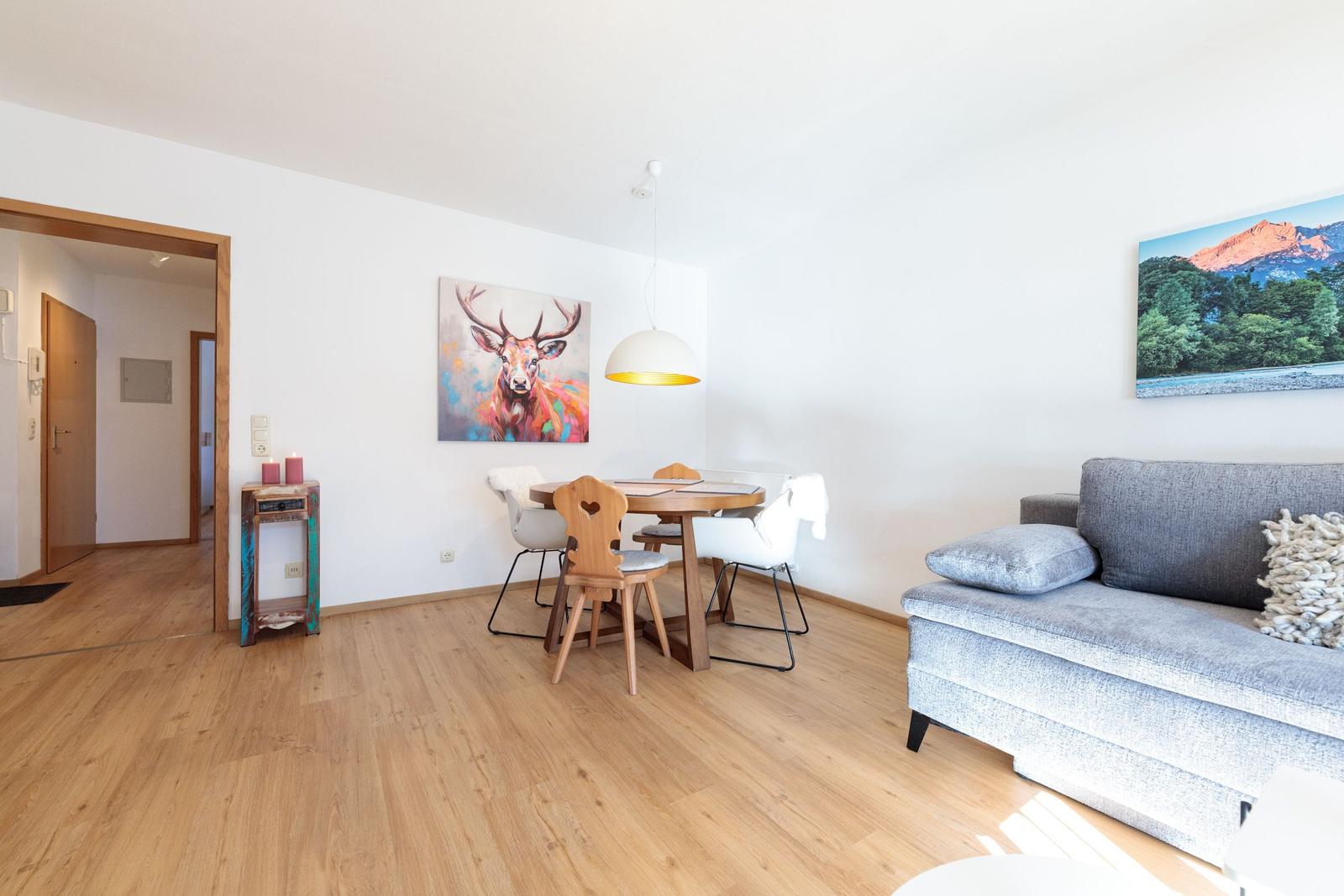 Wohn- und Essbereich mit Sofa, Tisch und Wandbildern.