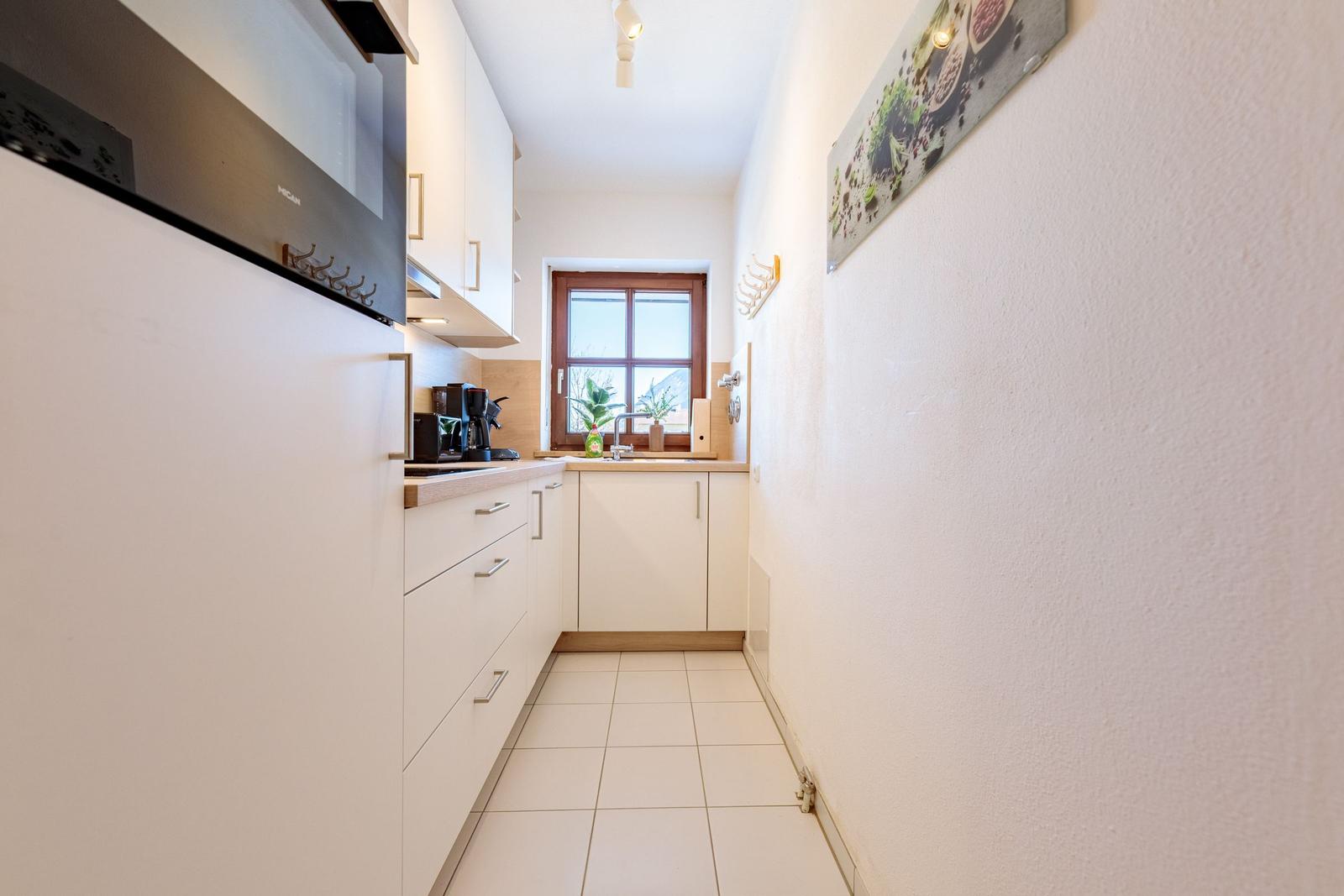 Küche mit weißen Schränken, Fenster und Spüle.
