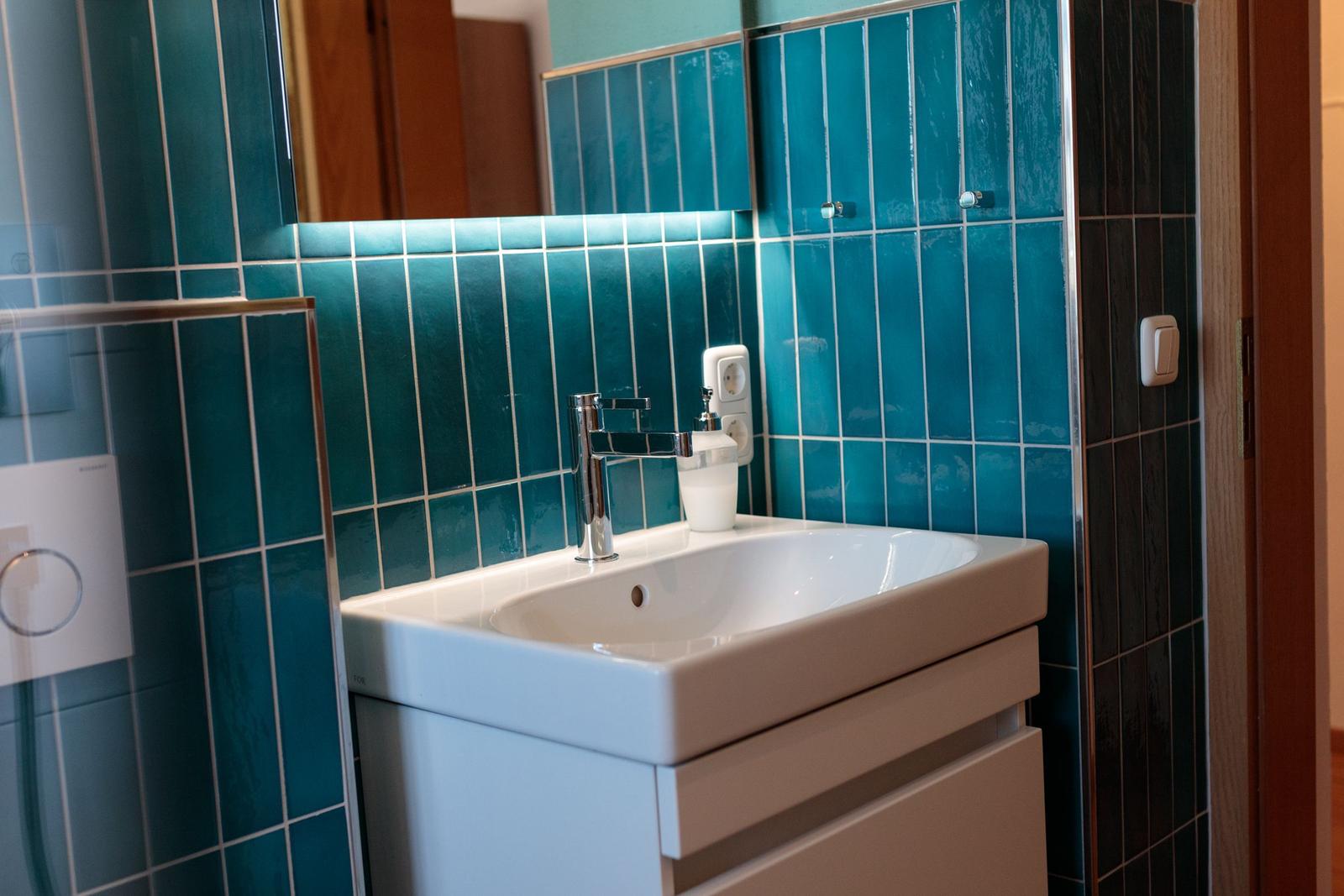 Badezimmer mit blauen Fliesen, Waschbecken und Spiegel.