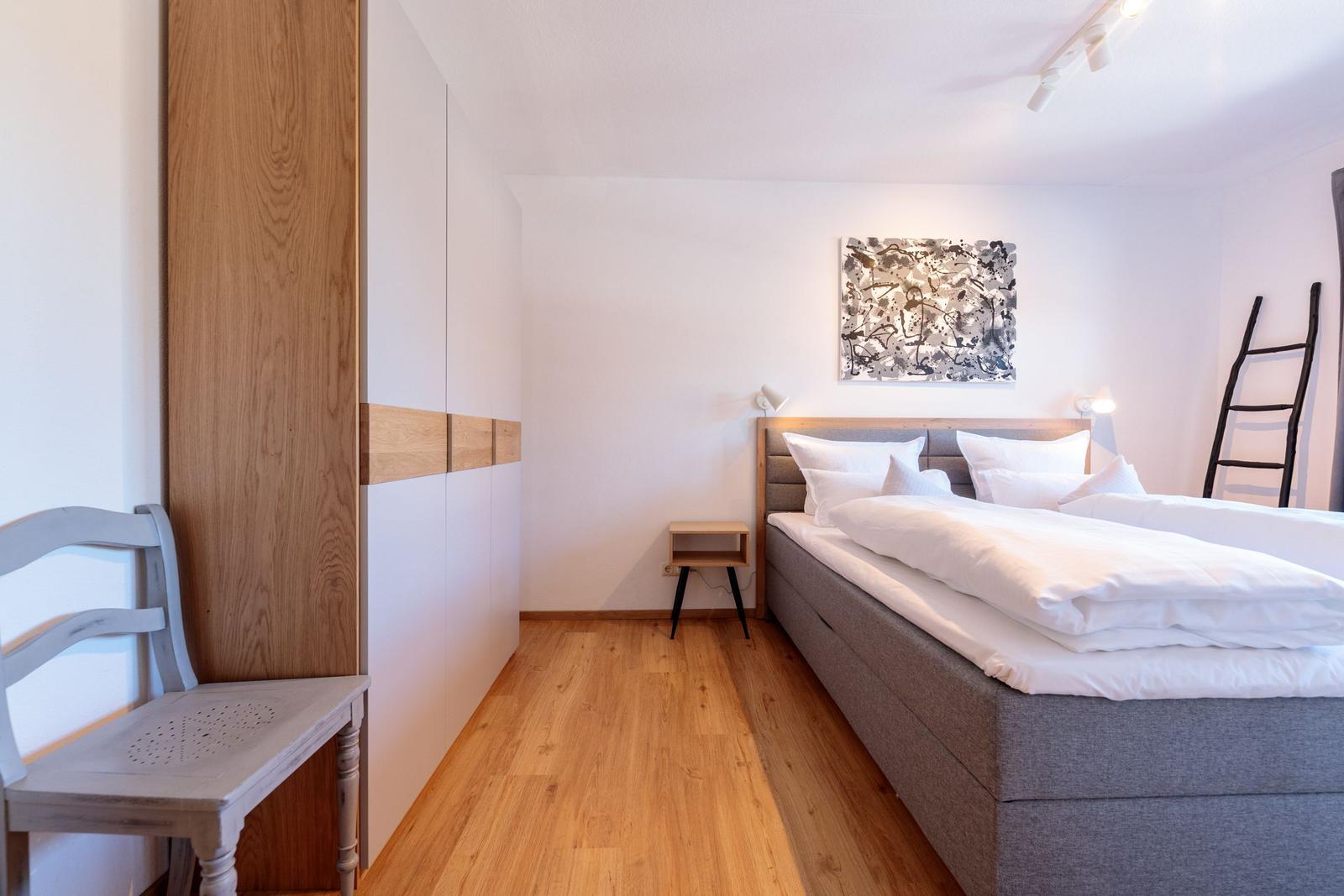 Schlafzimmer mit Bett, Nachttisch, Wandbild und Holzboden.