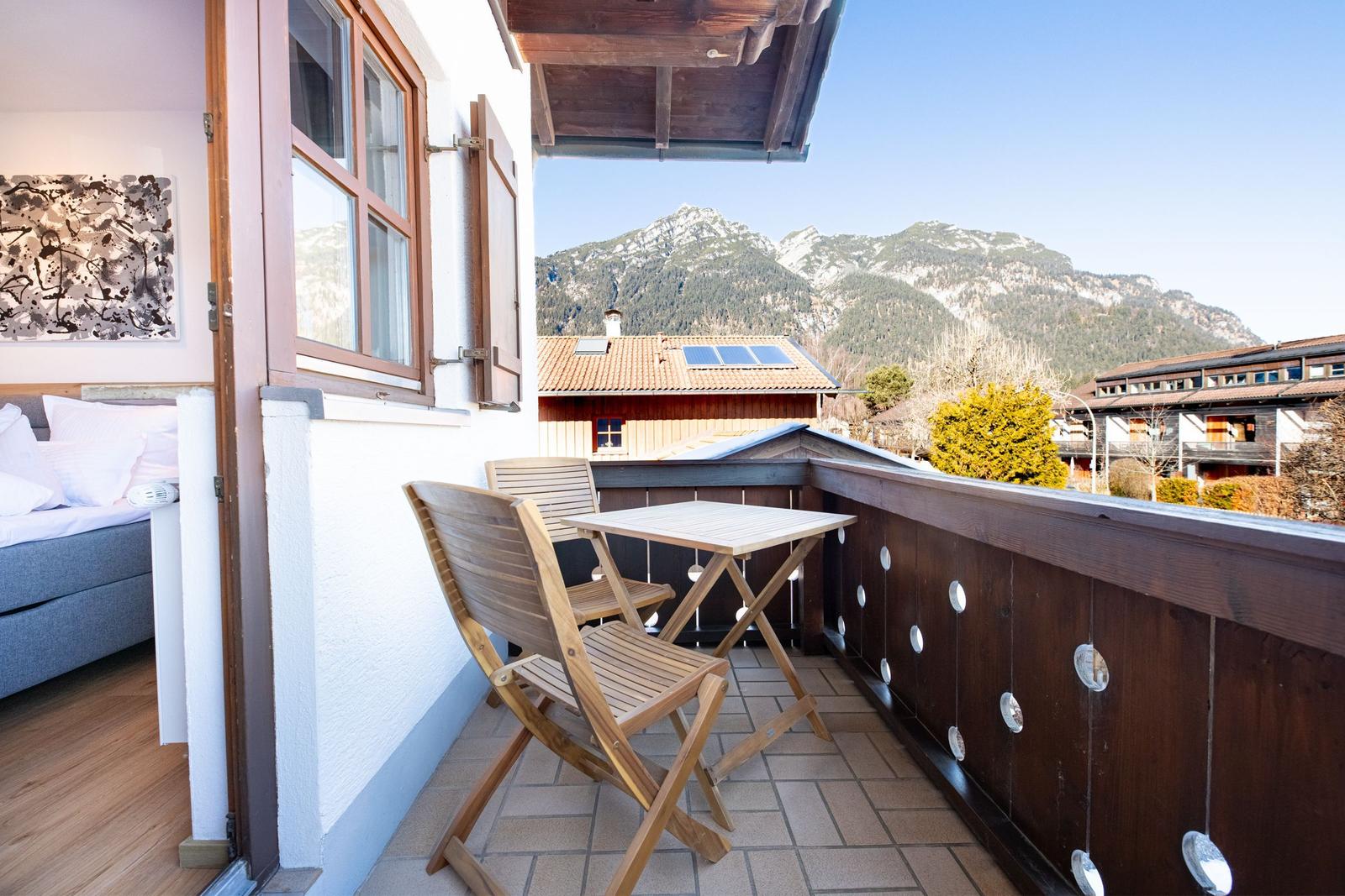 Terrasse mit Tisch und Stühlen, Blick auf Berge und Dächer.