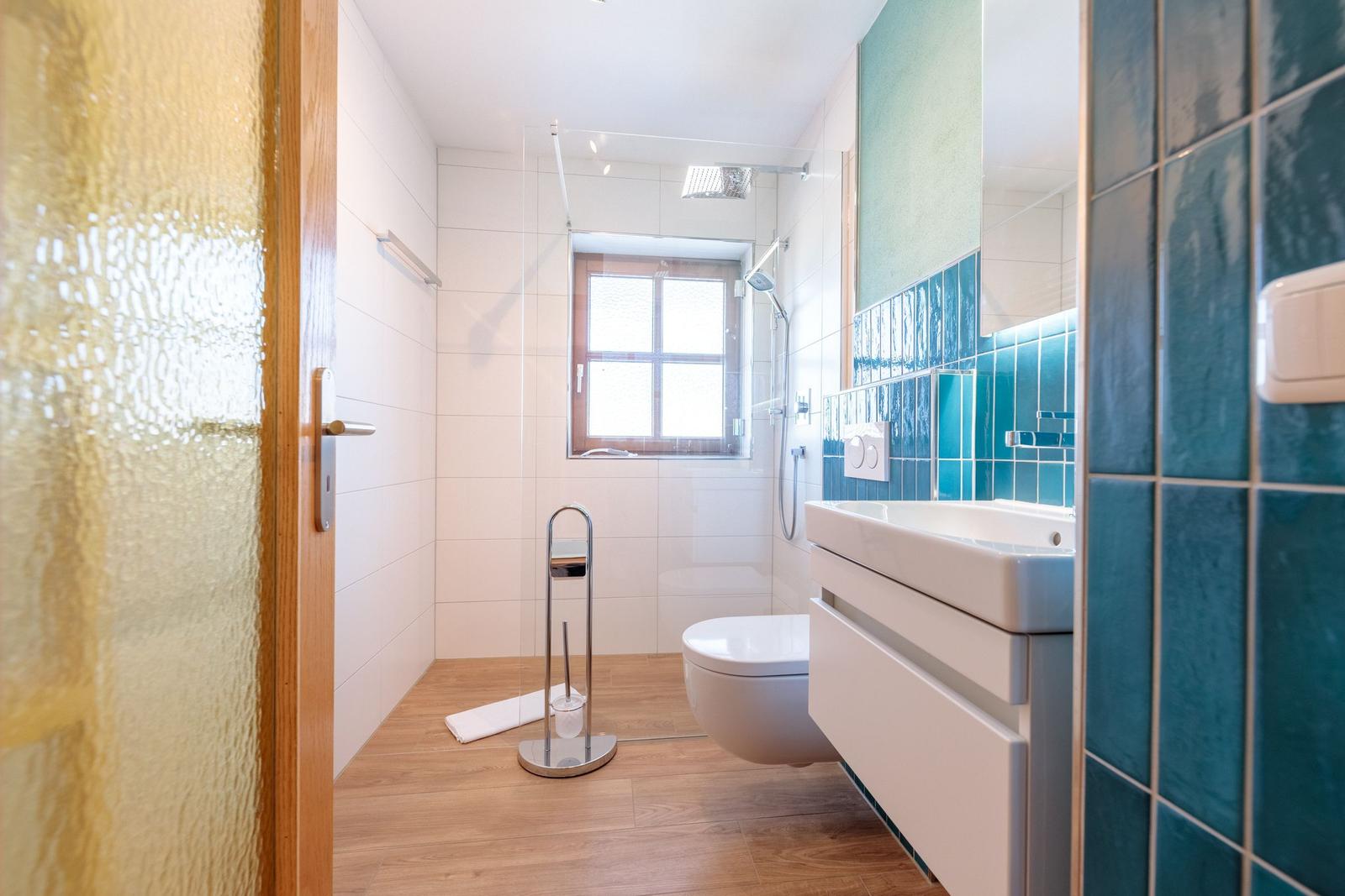 Badezimmer mit Dusche, Toilette und Waschbecken. Holzfußboden und blaue Fliesen.