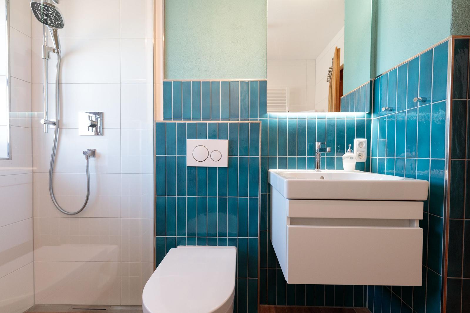 Badezimmer mit Dusche, Toilette und Waschbecken mit blauen Fliesen.