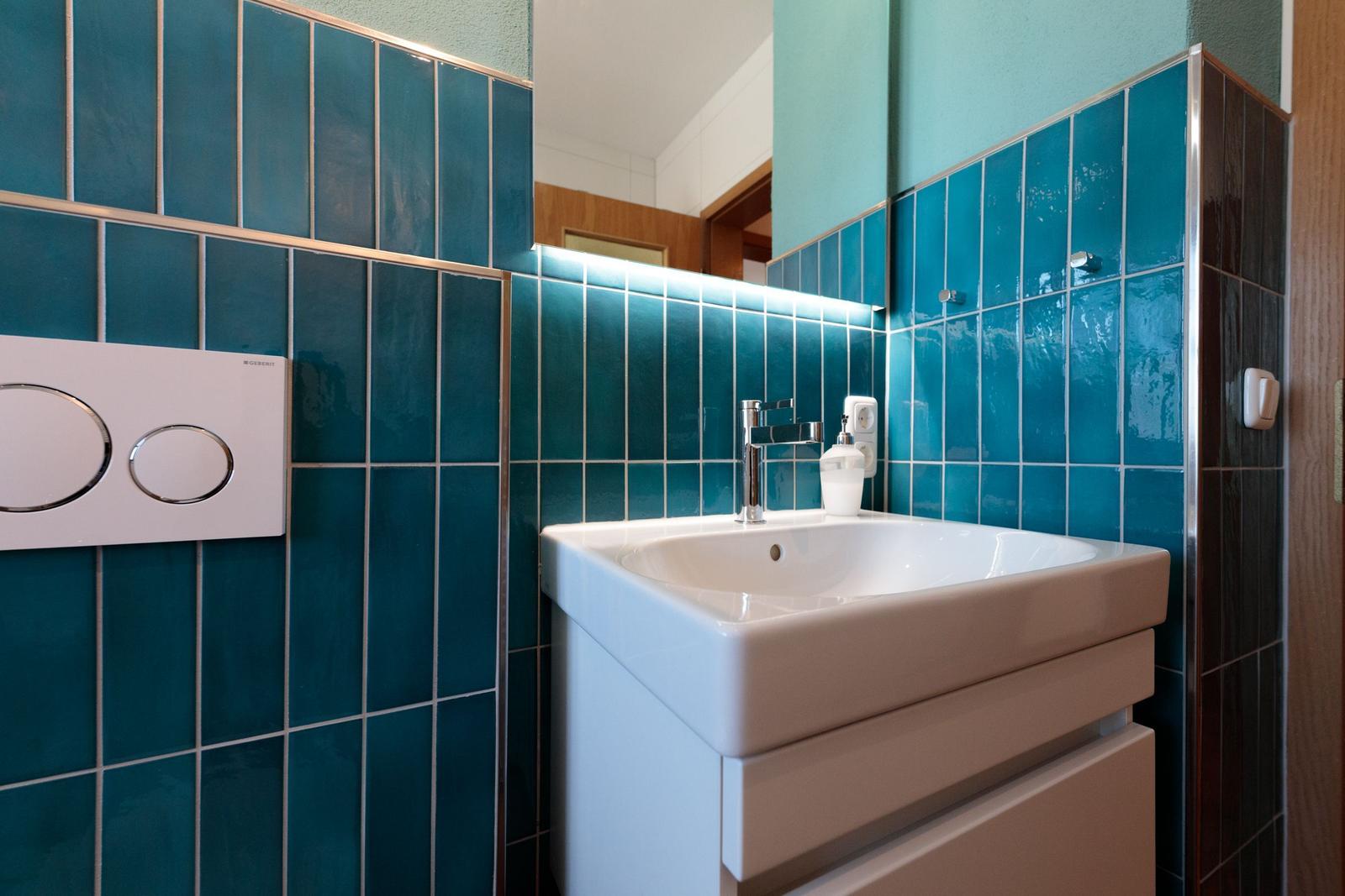 Badezimmer mit blauen Fliesen, Waschbecken und Spiegel.