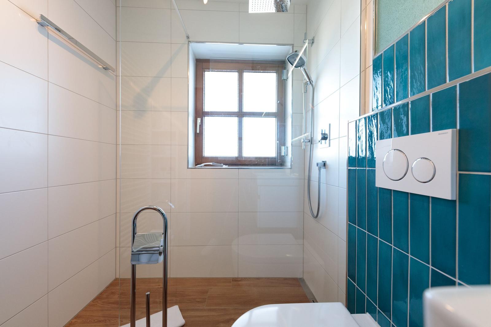 Badezimmer mit Dusche, Fenster und blauen Fliesen.
