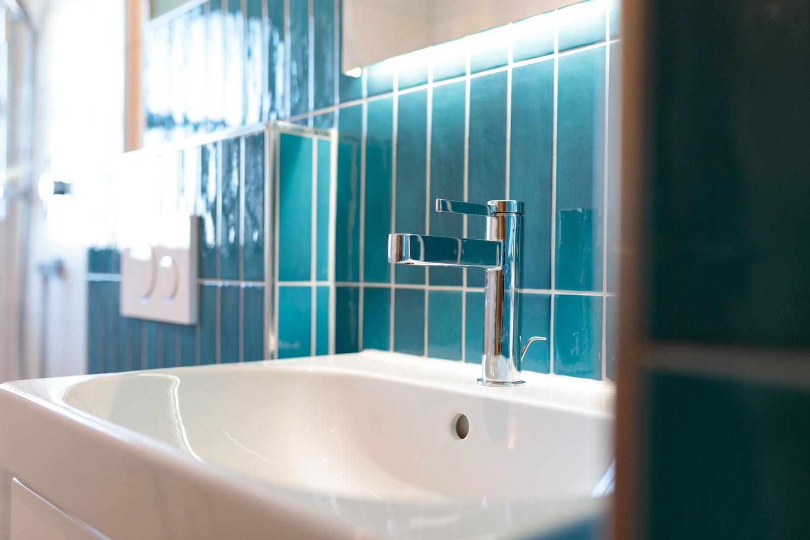 Waschbecken mit modernem Wasserhahn und blauen Fliesenwand.