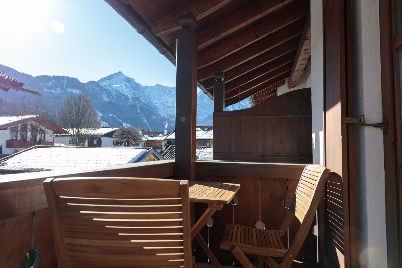 Holzterrasse mit Tisch und Stühlen, Blick auf schneebedeckte Berge und Dächer.