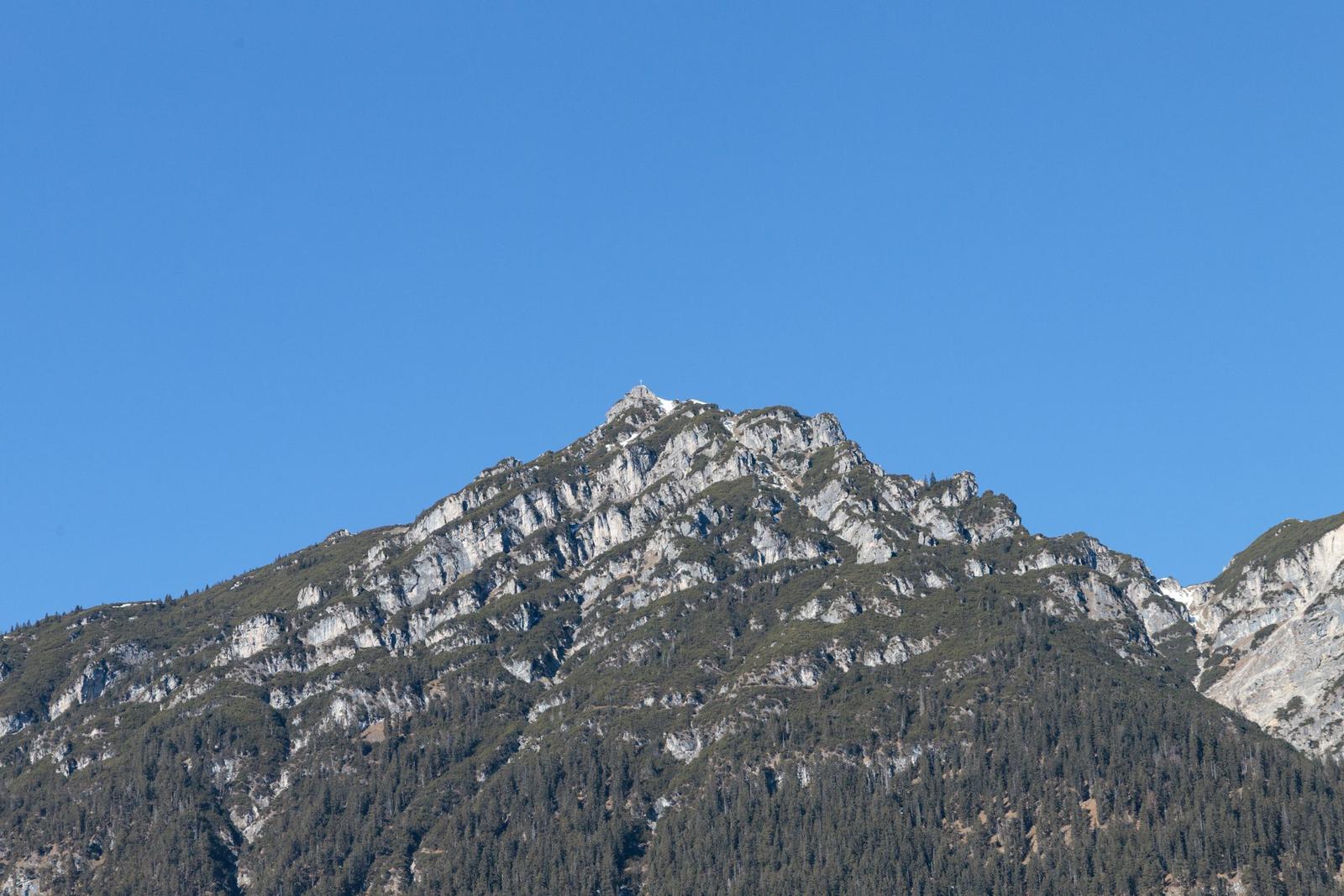 Hoher Berg mit Felsformationen und Wald unter blauem Himmel