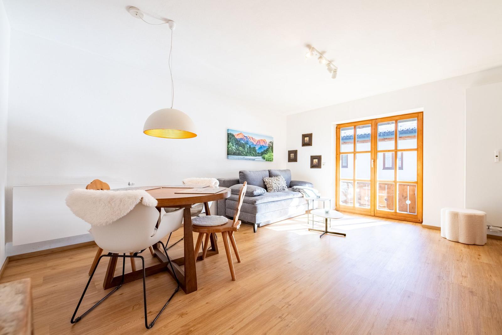 Essbereich mit Tisch und Stühlen, Sofa und Holztüren zum Balkon.