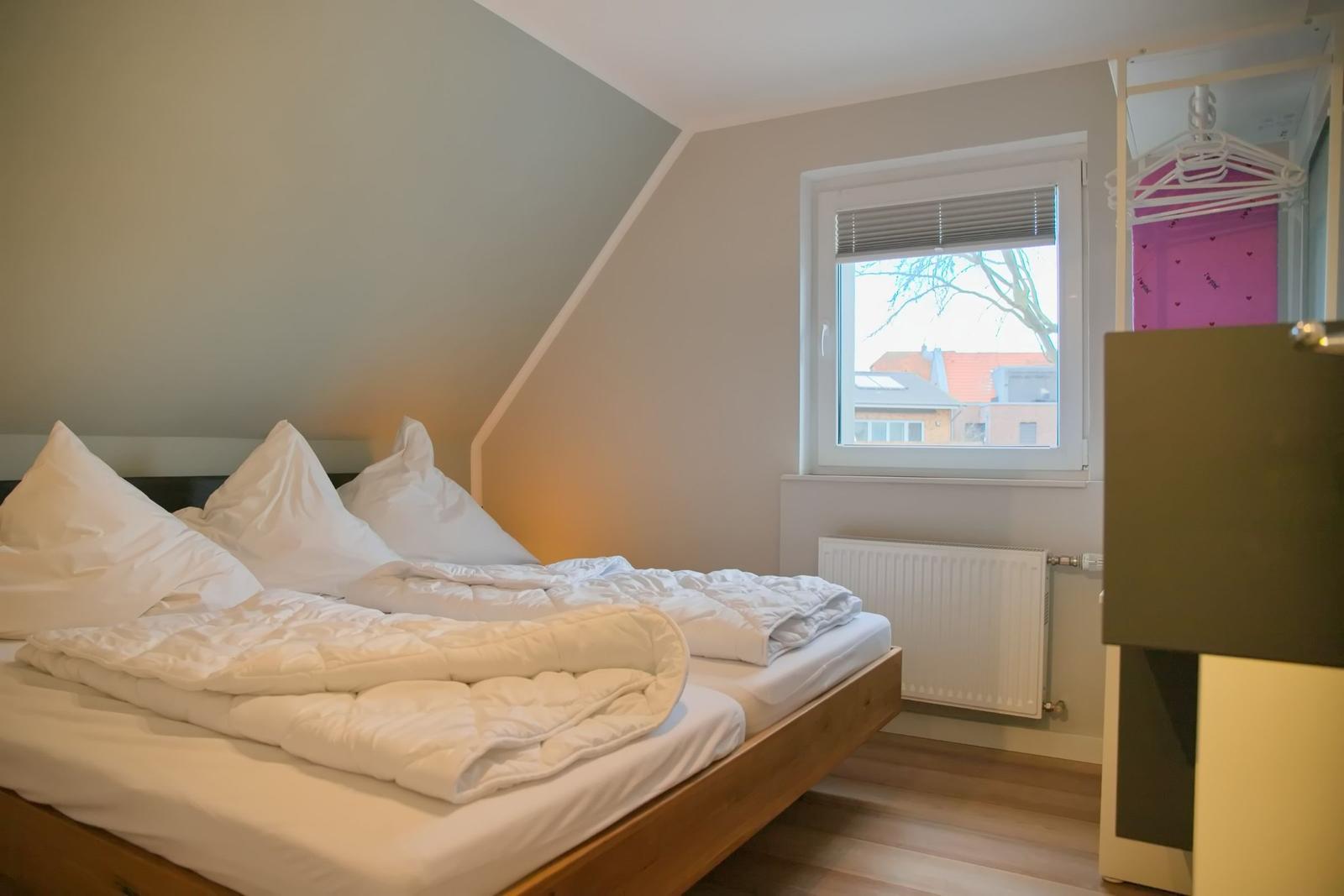 Schlafzimmer mit Dachschrägen, Bett und Fenster mit Blick auf Dächer.