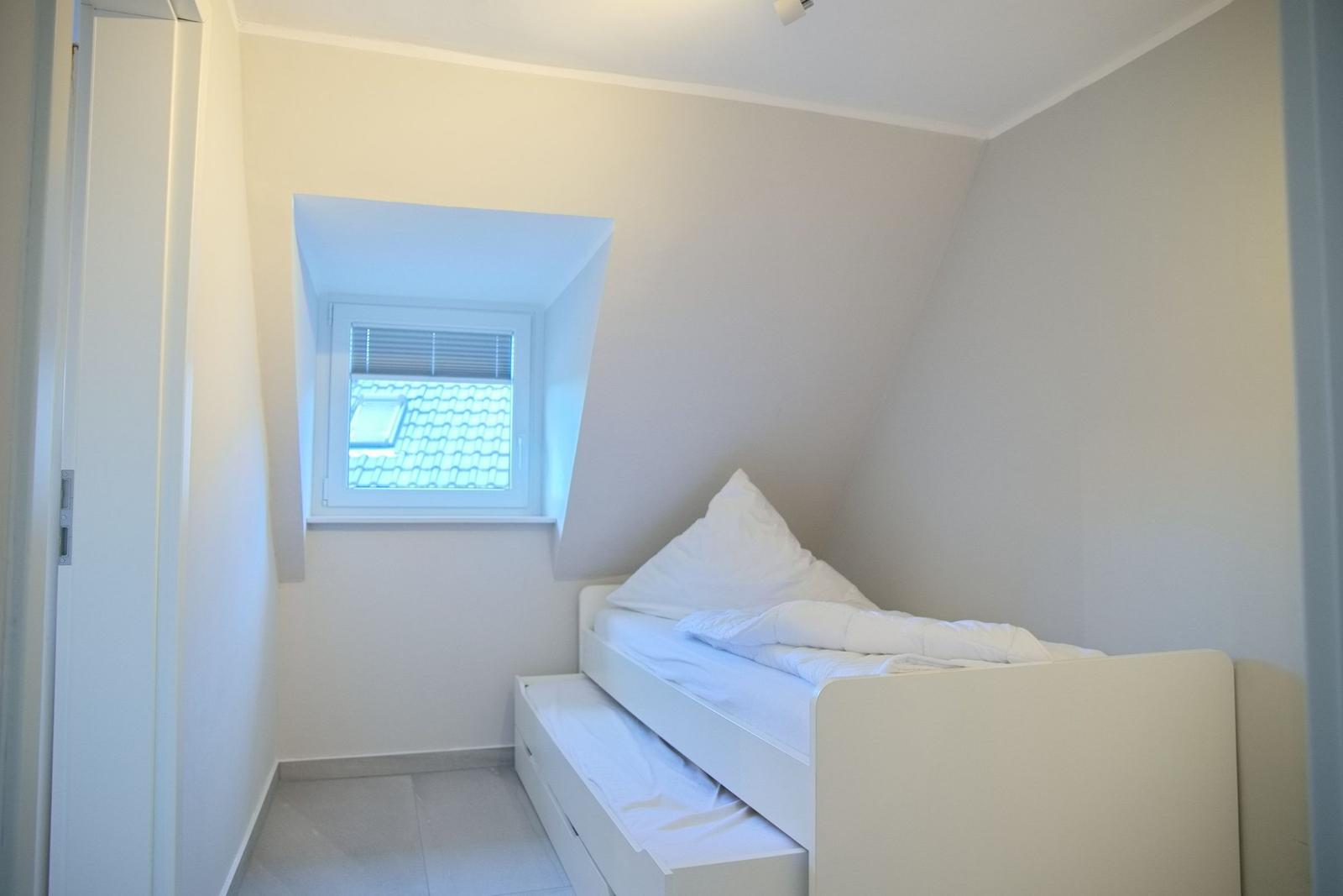 Schlafzimmer mit Dachschrägen, weißem Bett und Fenster mit Blick auf Dach.