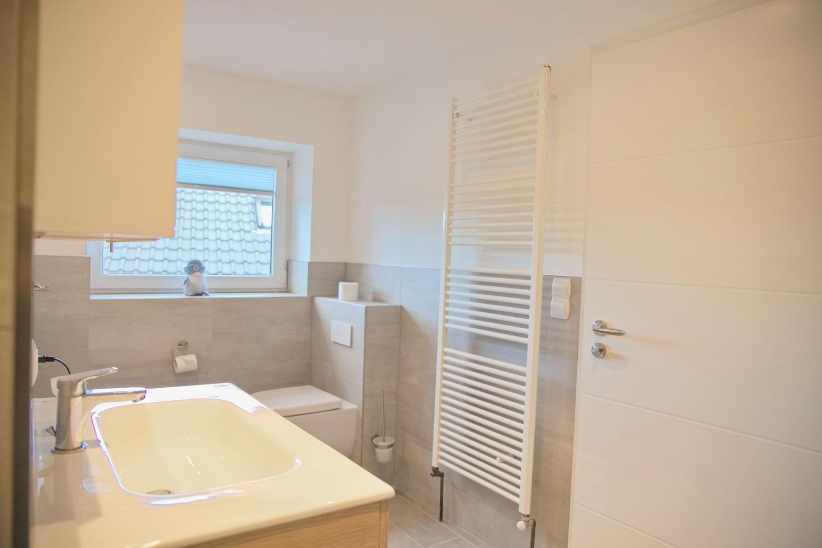 Badezimmer mit Waschbecken, Toilette und Heizkörper. Fenster mit Blick auf Dach.