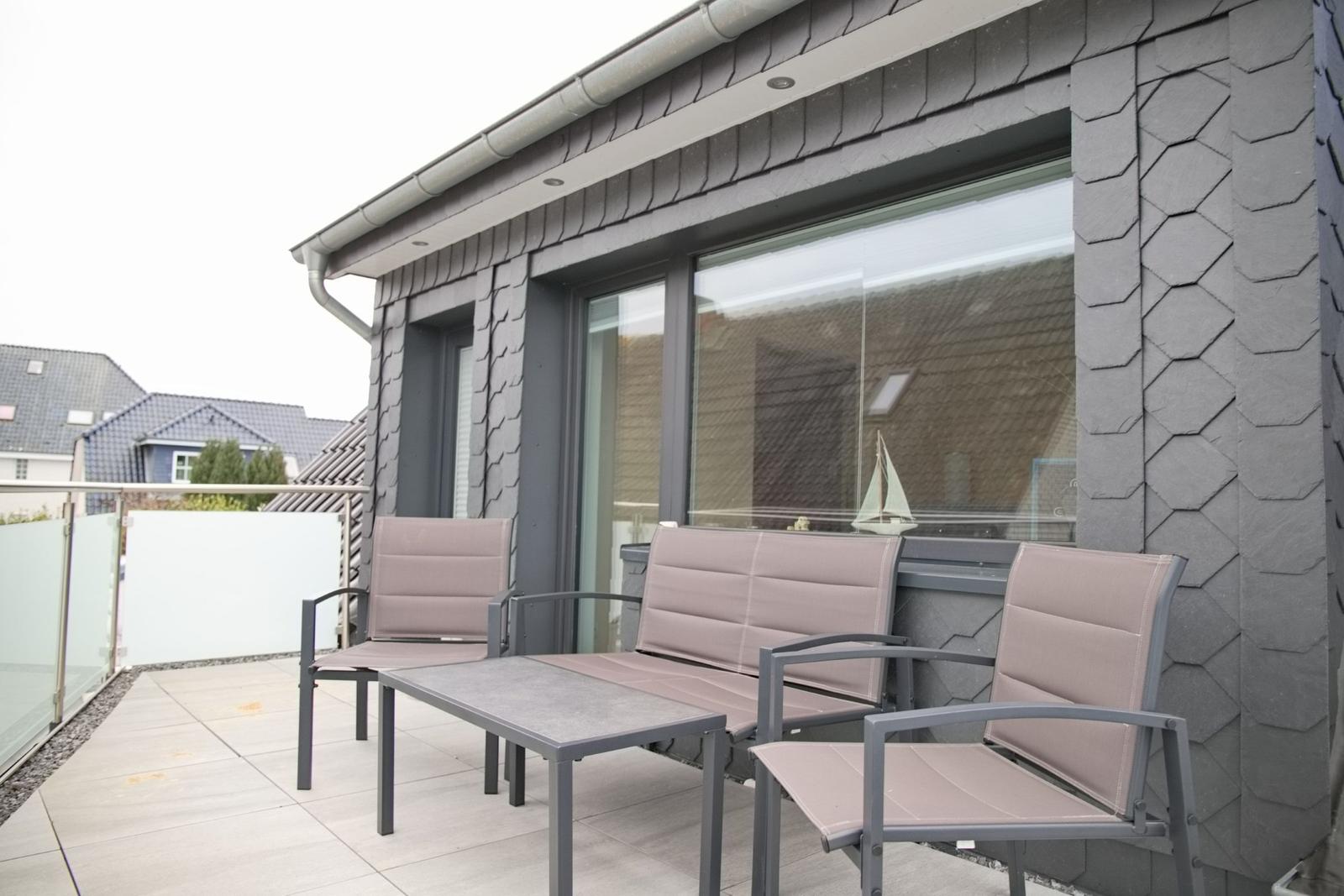 Terrasse mit Sitzgruppe und Glasgeländer. Modernes Haus mit großen Fenstern.