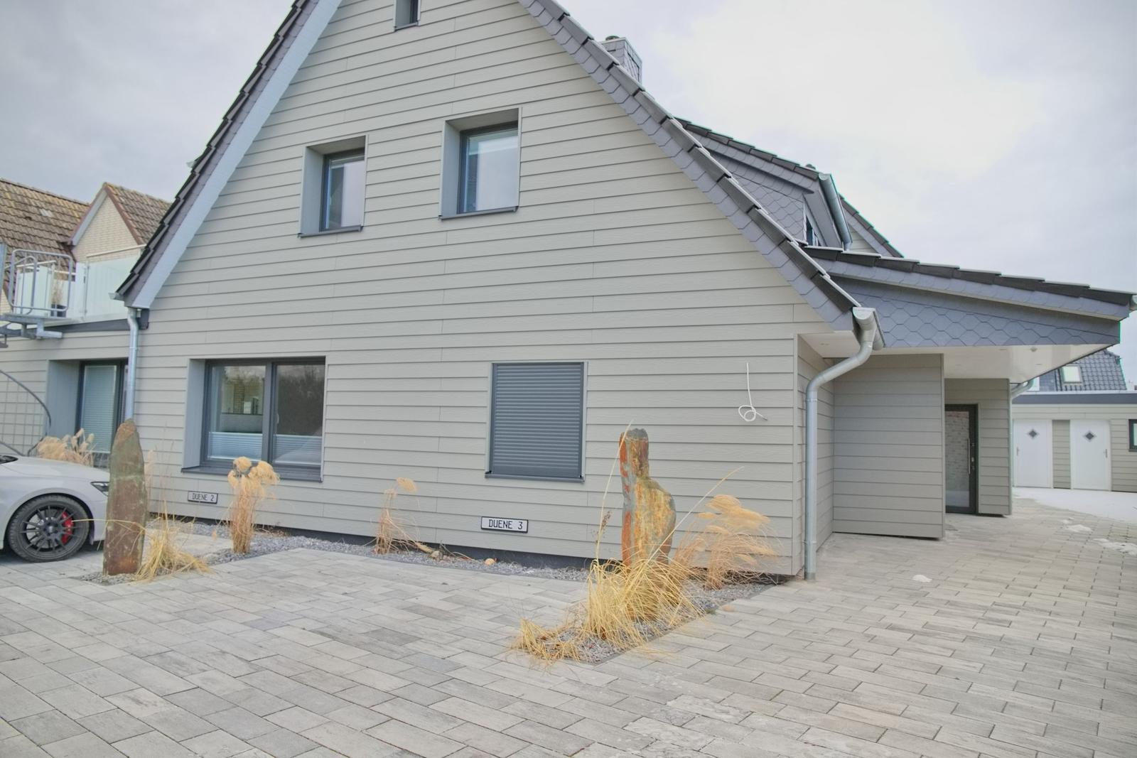 Moderne Ferienwohnung mit grauer Fassade und gepflastertem Vorplatz.