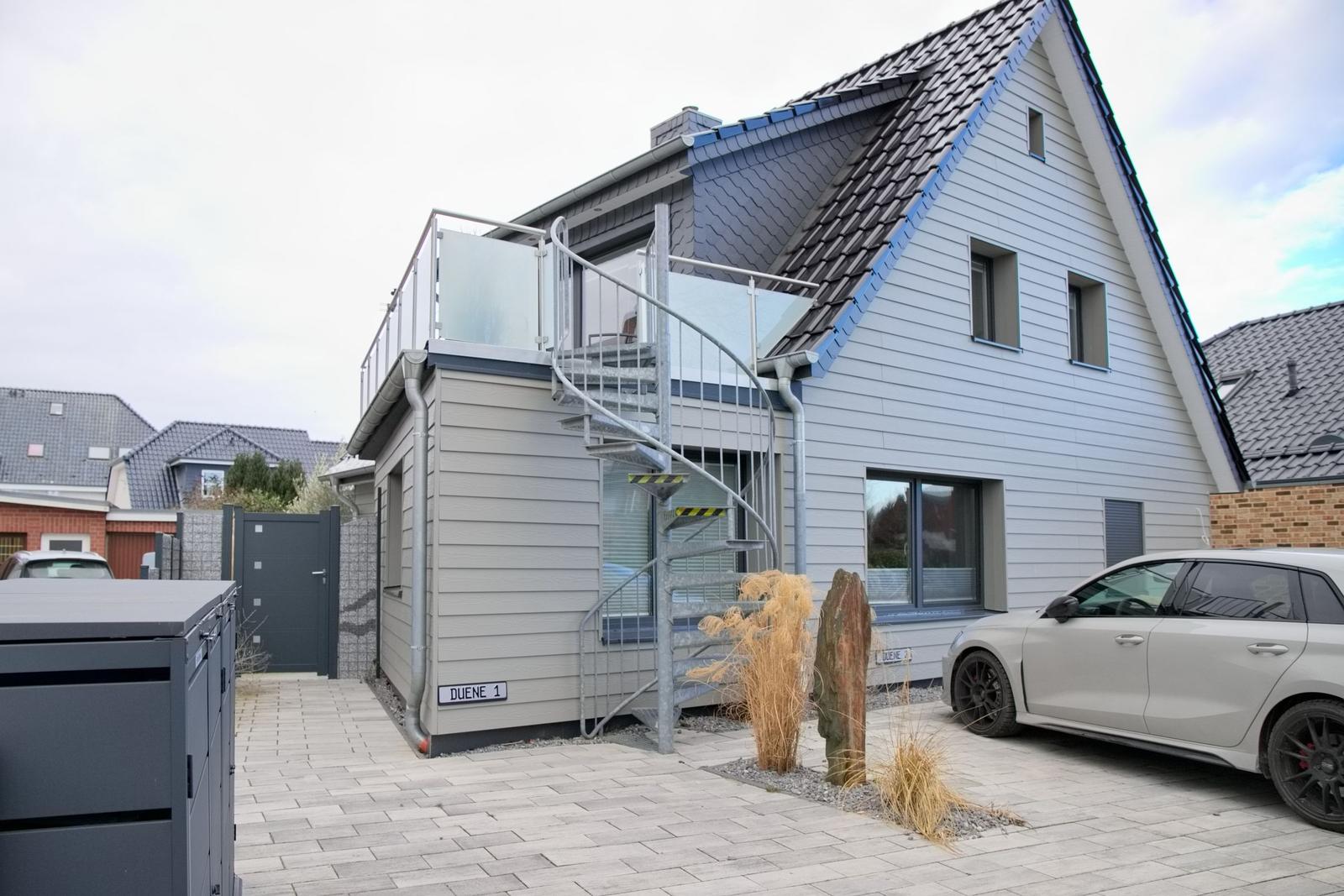 Moderne Villa mit Dachterrasse und spiralförmiger Außentreppe. Parkplatz mit gepflastertem Hof.