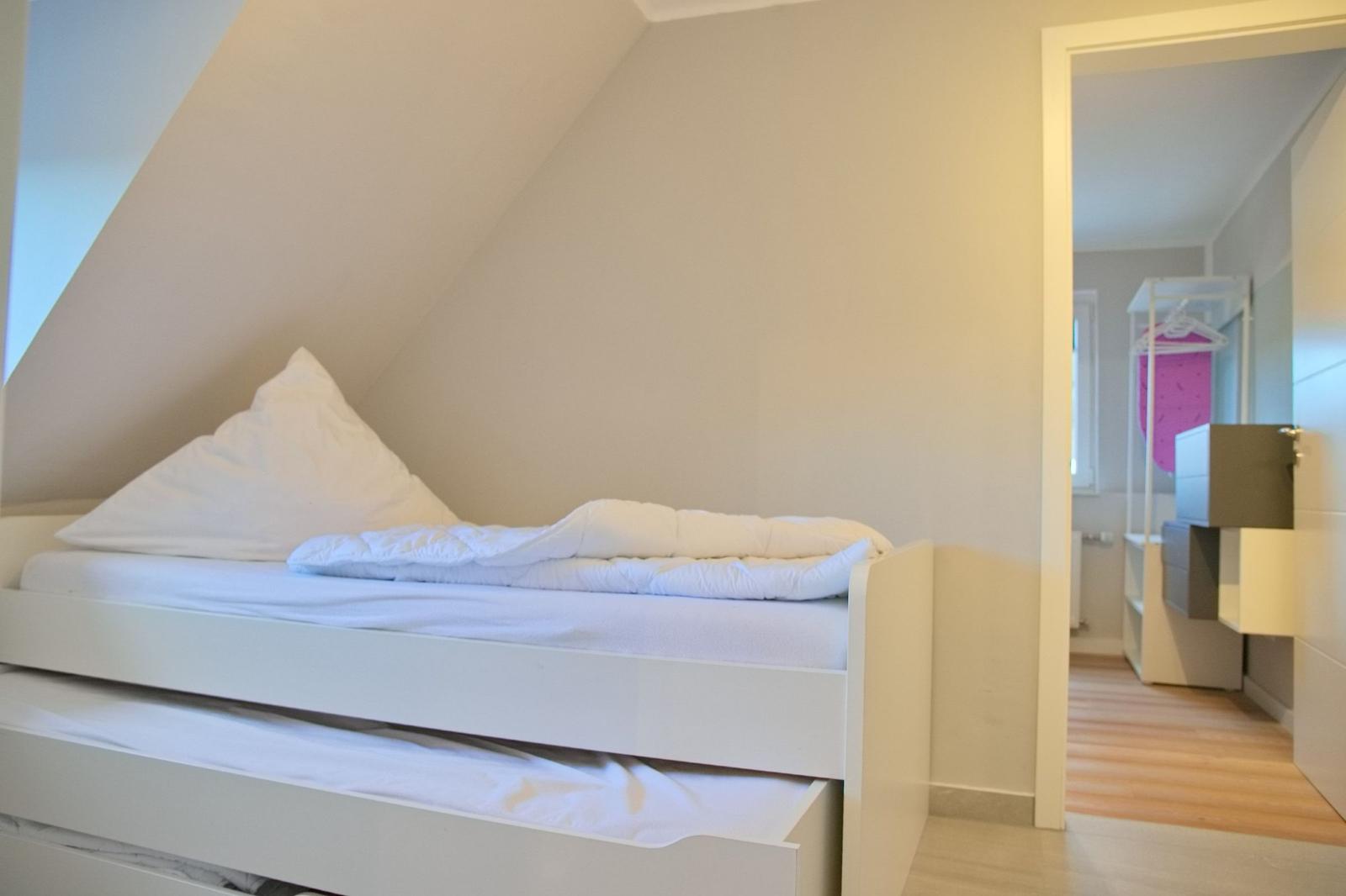 Schlafzimmer mit weißem Bett und Schiebetüren unter Dachschrägen.