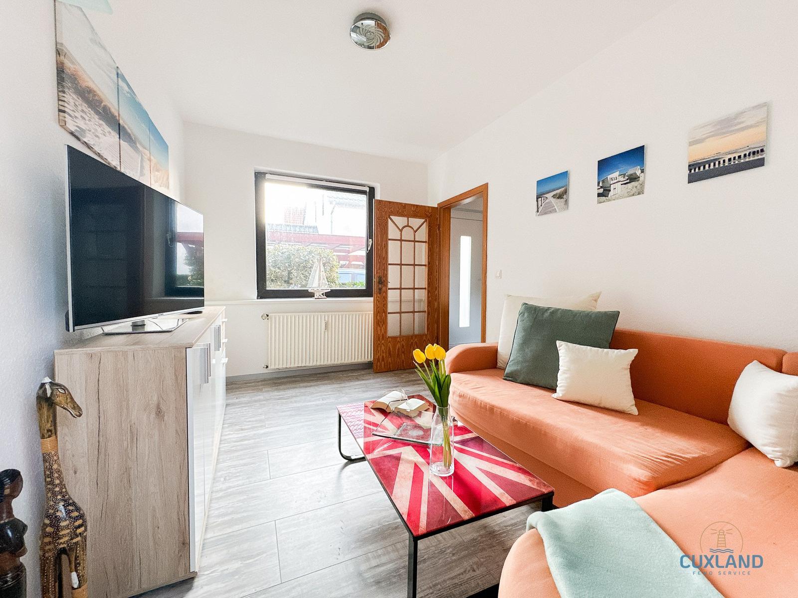 Wohnzimmer mit orangefarbenem Sofa, TV und Fenster.