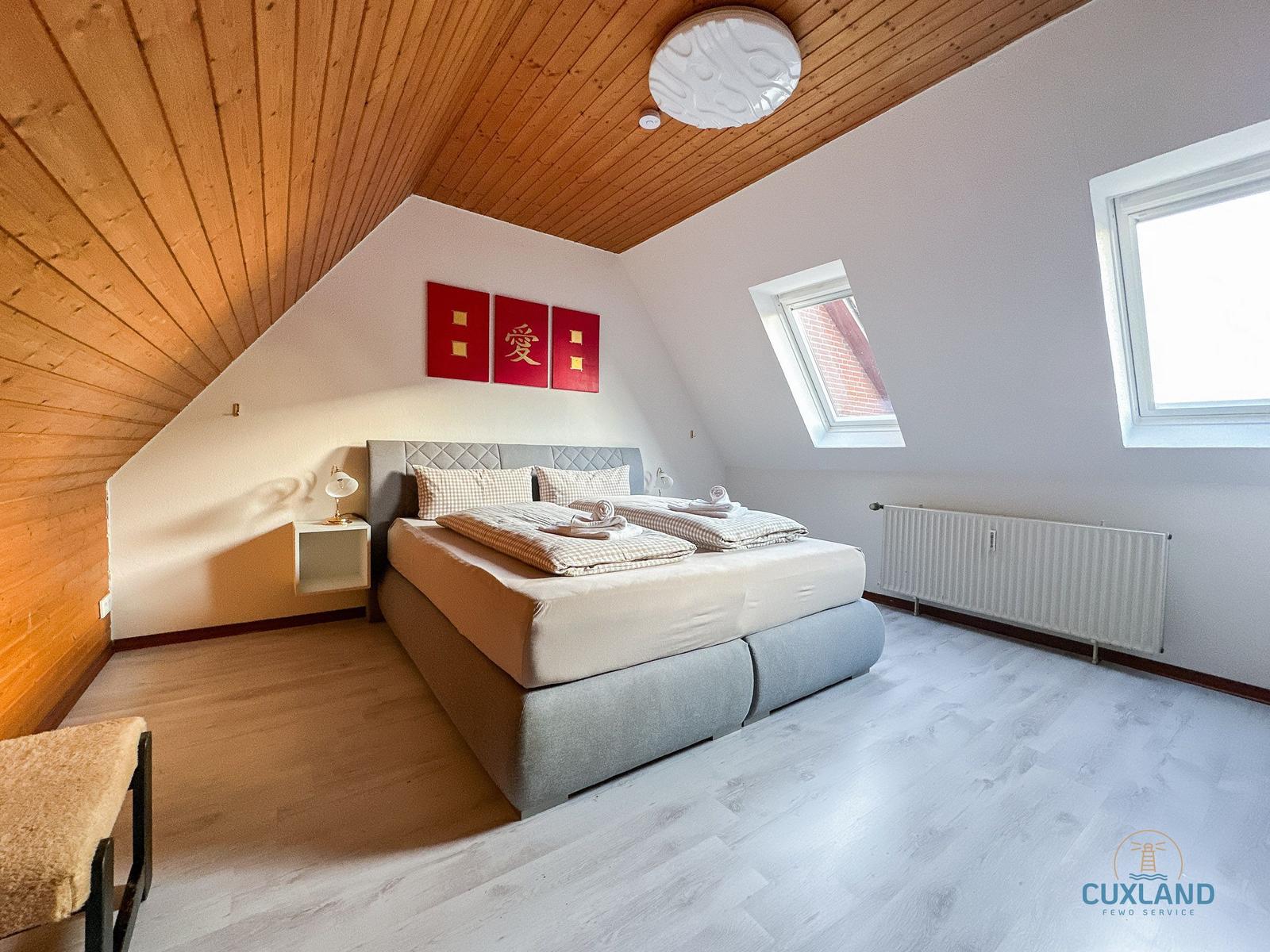 Schlafzimmer mit Dachschrägen, Bett, Fenster und Holzdecke.