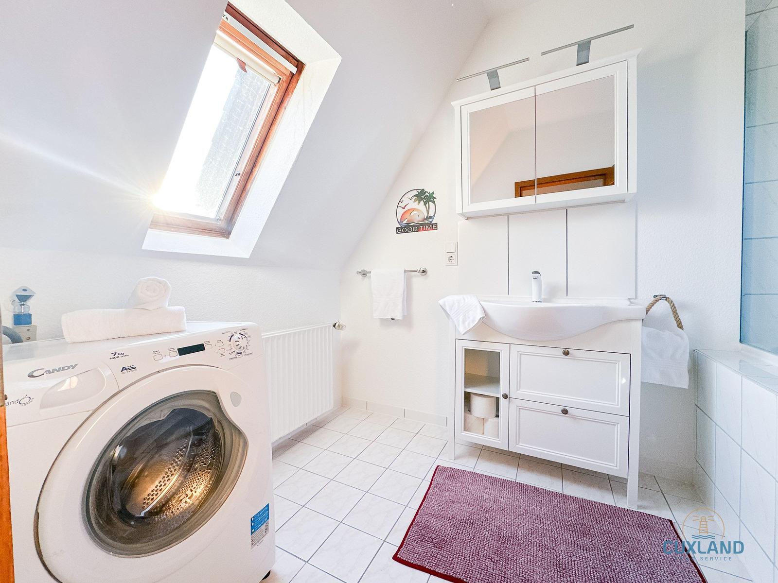 Badezimmer mit Waschmaschine, Waschtisch und Dusche unter Dachschrägen.