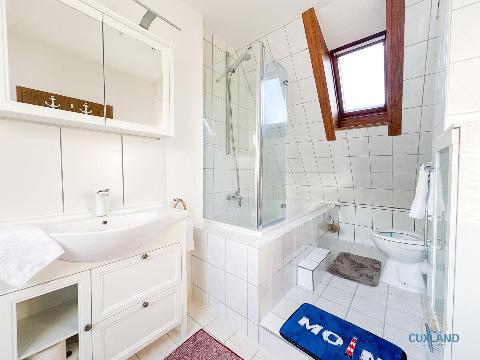 Badezimmer mit Dusche, Toilette und Waschbecken. Holzfenster und maritime Dekoration.