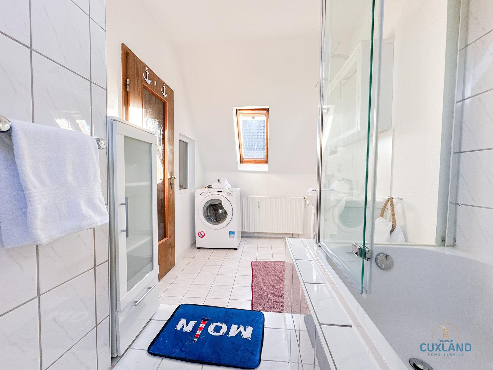 Badezimmer mit Badewanne, Dusche, Waschmaschine und Fenster.