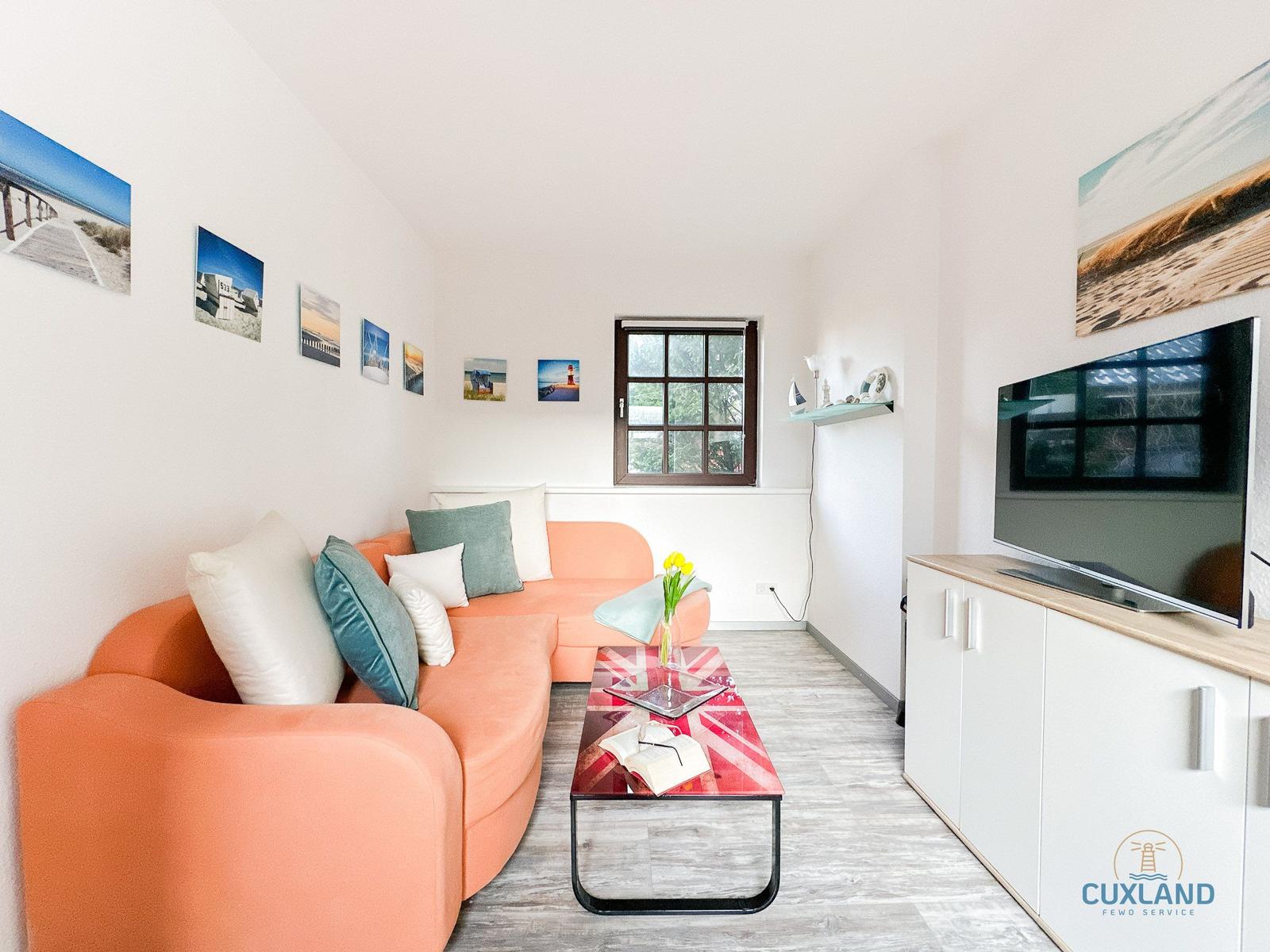 Wohnzimmer mit orangefarbenem Sofa, Glas-Tisch und Fernseher.
