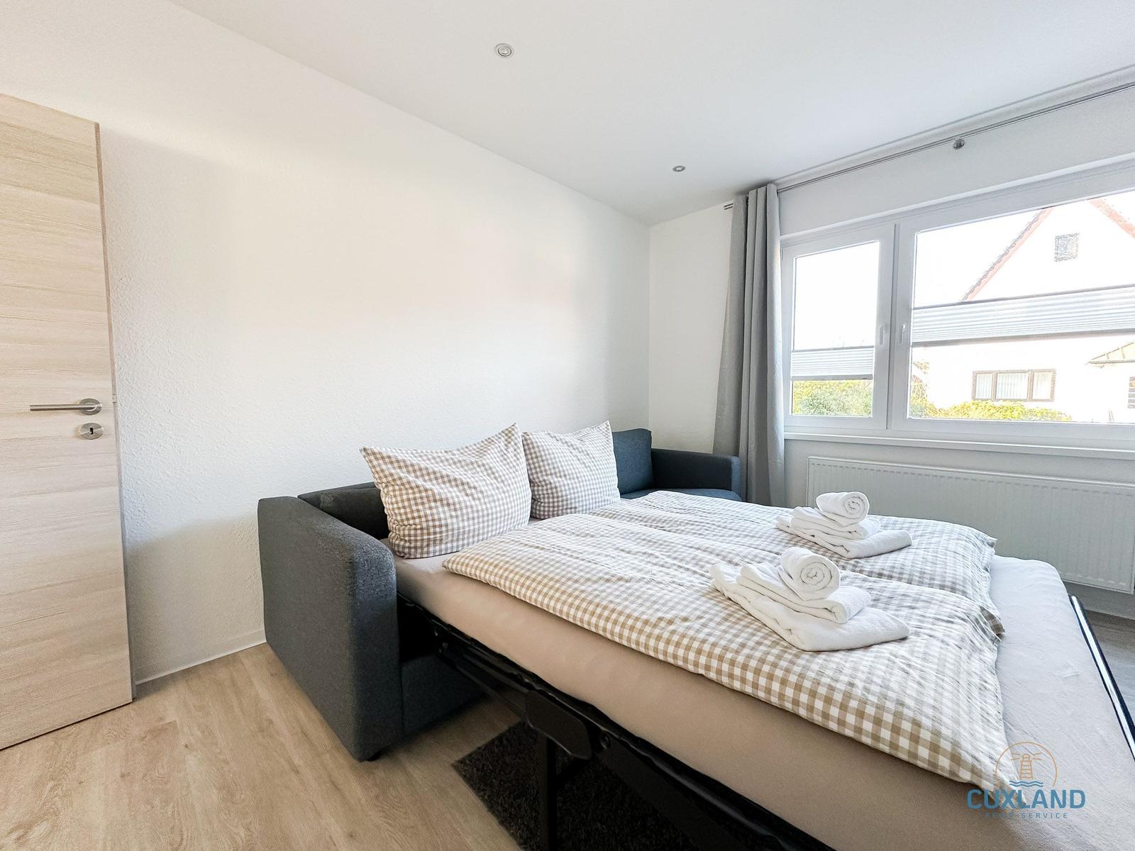 Schlafzimmer mit Schlafcouch, Fenster und Holzboden.