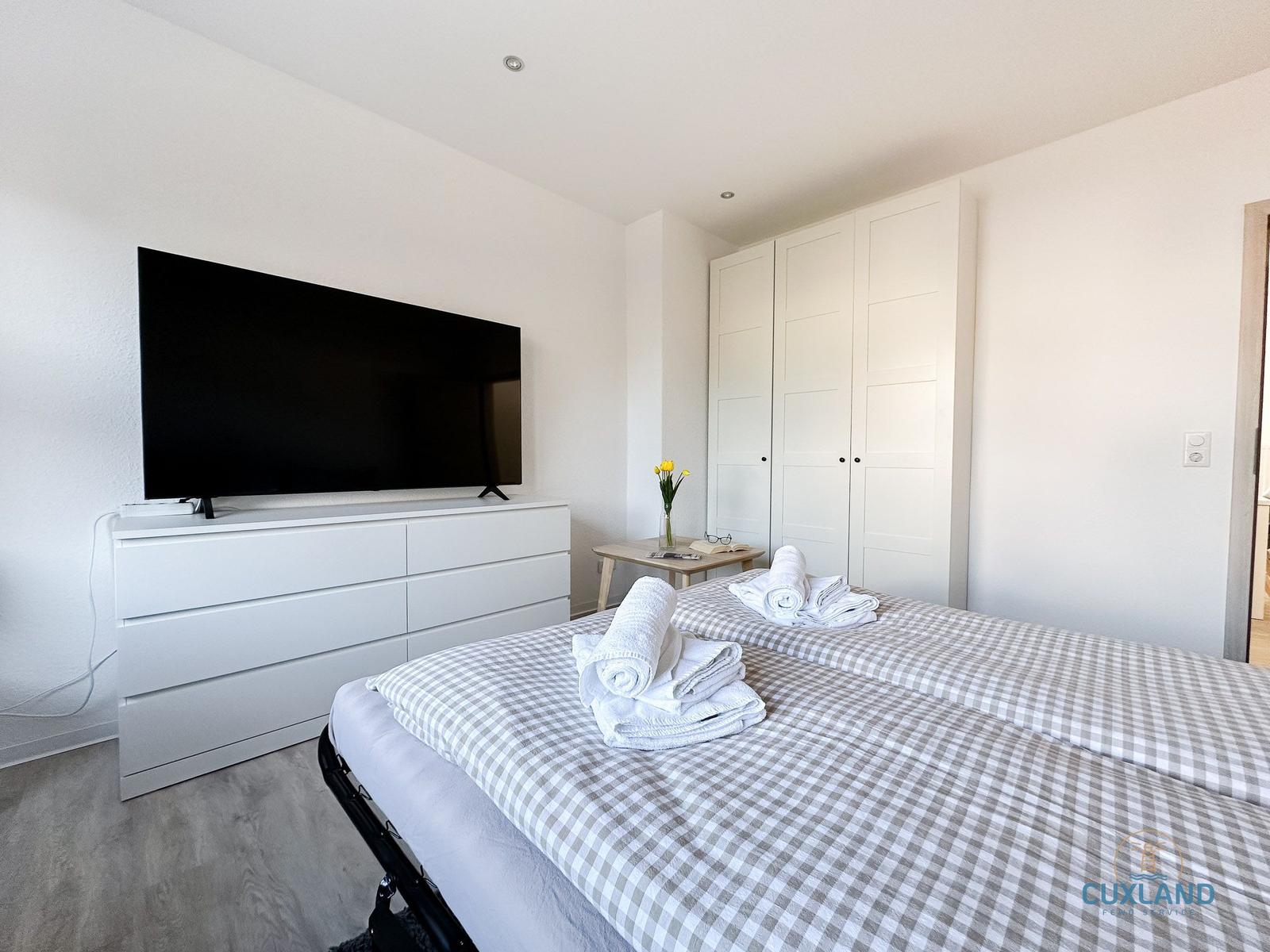 Schlafzimmer mit Bett, Fernseher und Kleiderschrank.