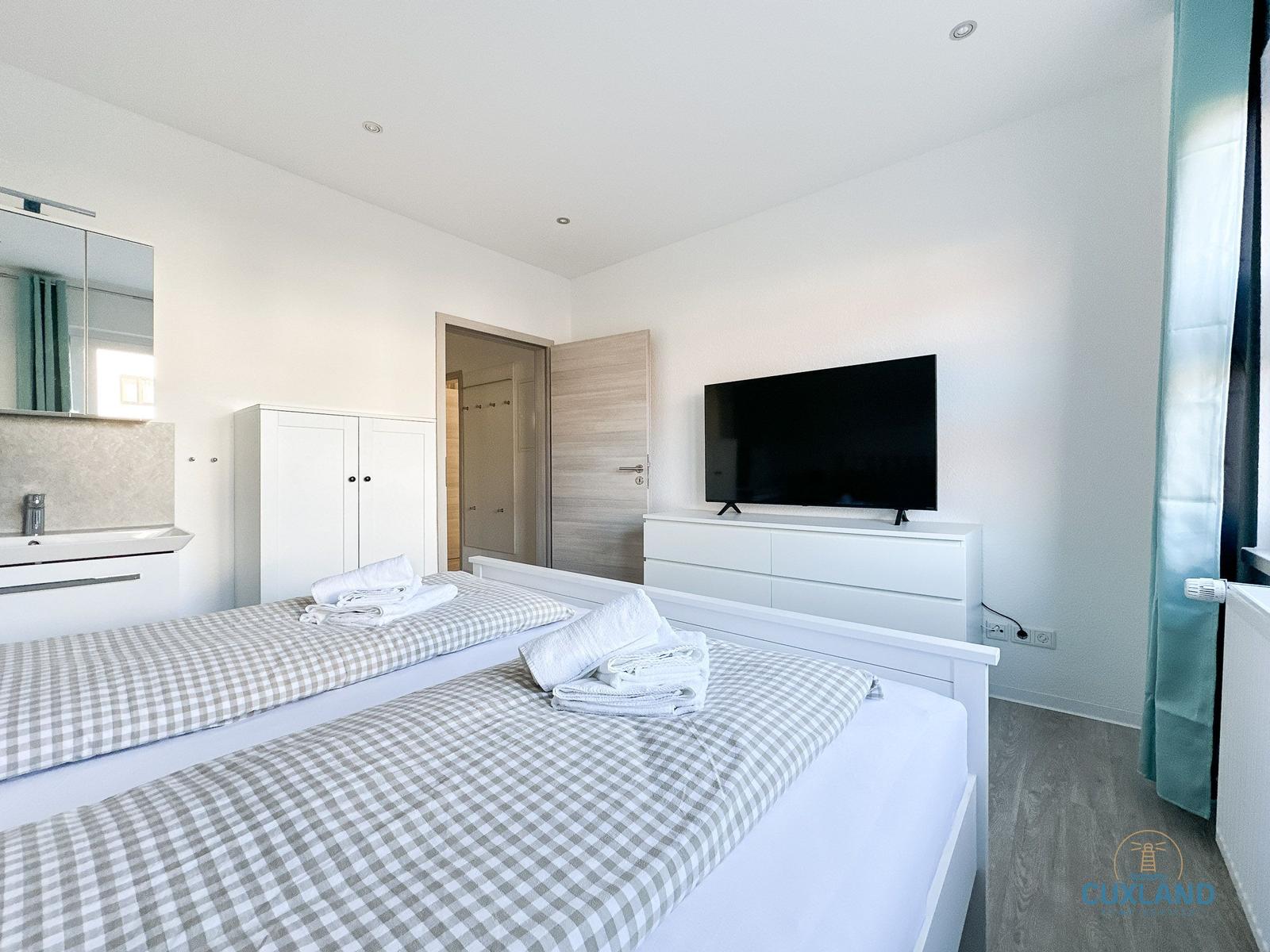 Zwei Betten mit Handtüchern, Fernseher und Kleiderschrank im Schlafzimmer.