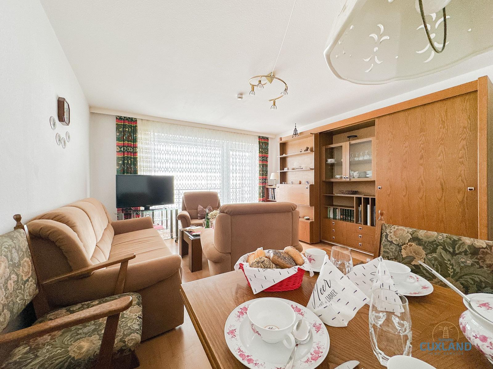 Wohn- und Essbereich mit Sofa, TV und Esstisch mit Tischwäsche.