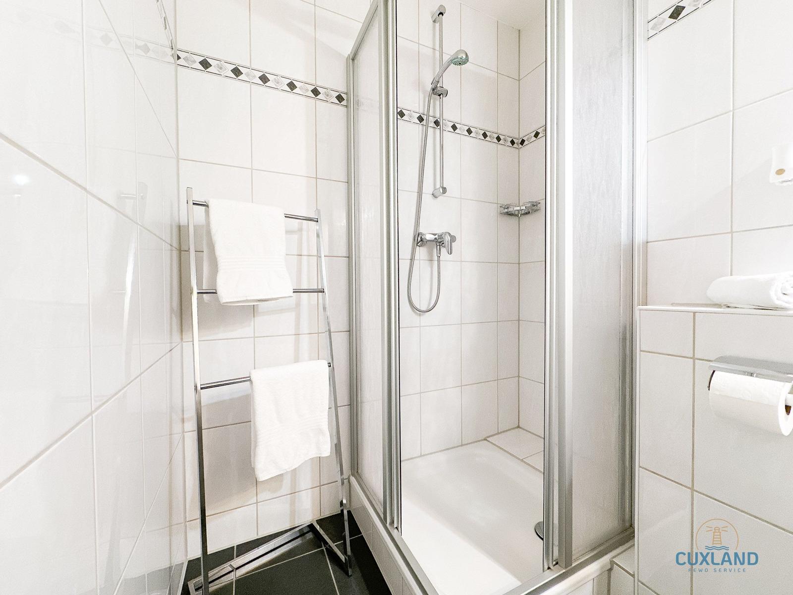 Bad mit Dusche, Handtuchhalter und Toilettenpapier.