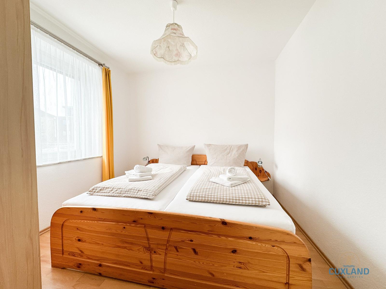 Schlafzimmer mit Holzbett, Fenster und Deckenleuchte.