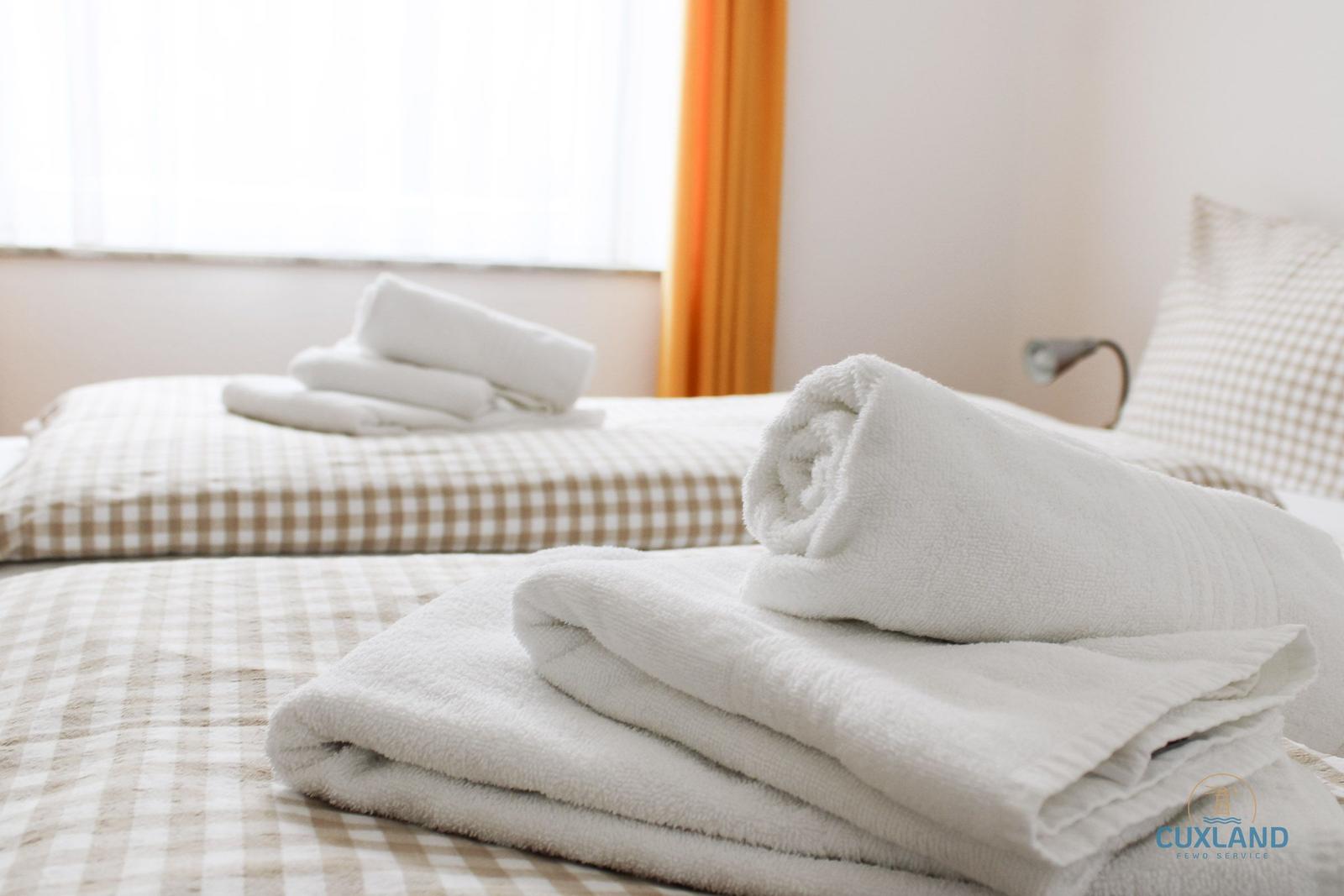 Zwei Betten mit karierten Bettwäschen und gefalteten weißen Handtüchern.