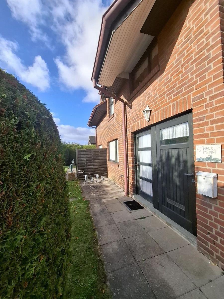 Haus mit rotem Ziegelstein, dunkler Tür und gepflastertem Weg neben Hecke.