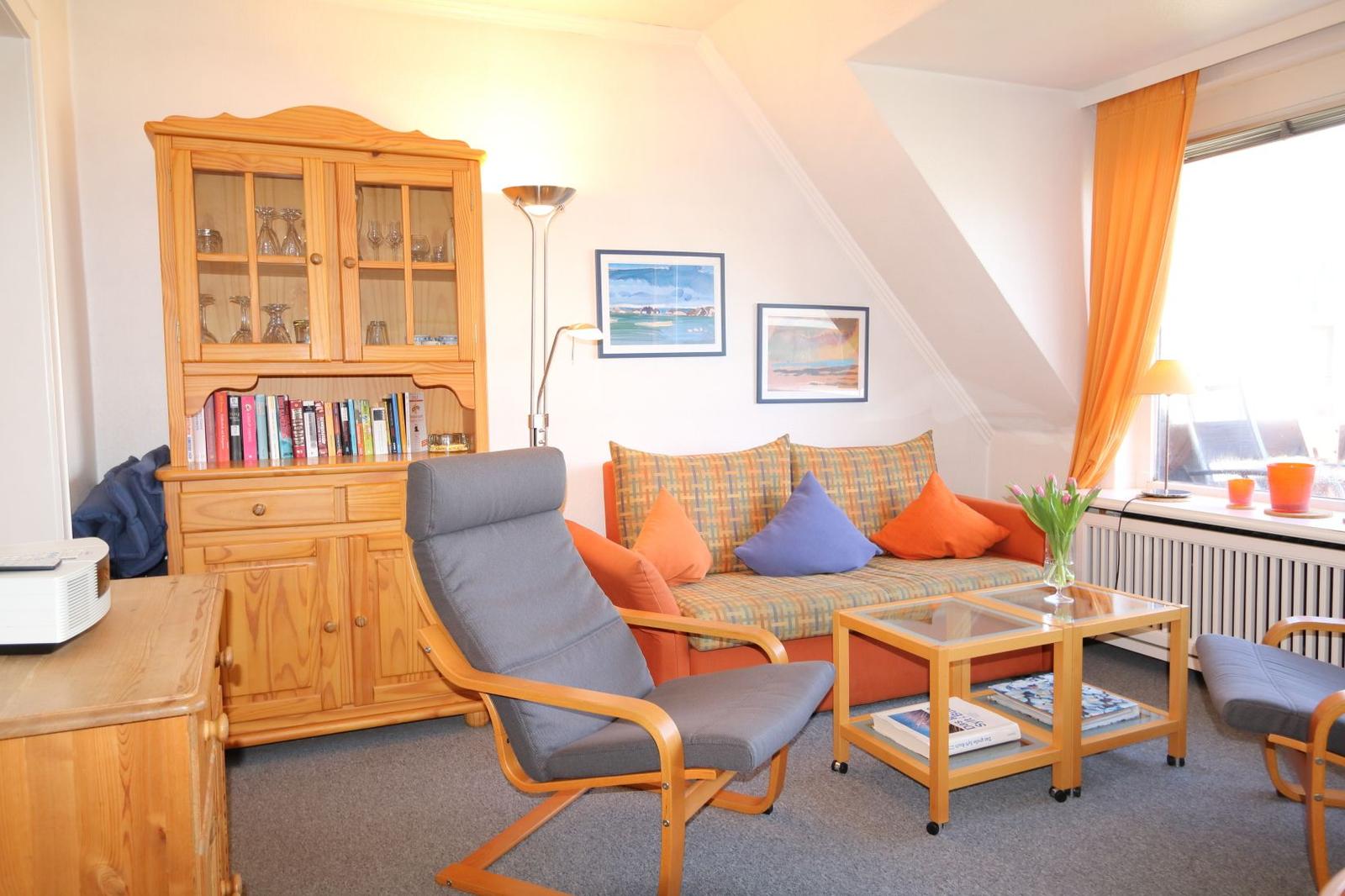 Wohnzimmer mit Sofa, Sessel und Holzmöbel. Fenster mit orangefarbenen Vorhängen.