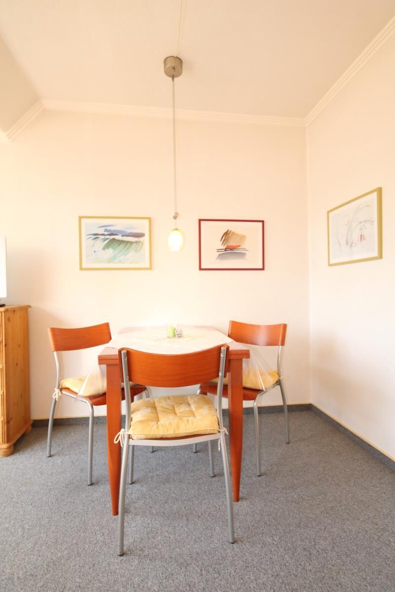 Esszimmer mit runden Tisch und vier Stühlen, Wandbilder und Pendelleuchte.