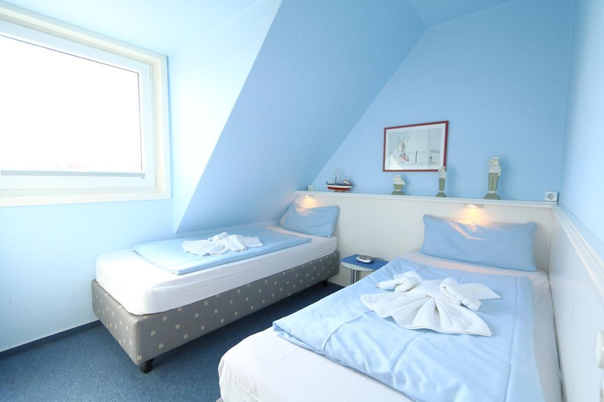 Zwei Betten in einem hellblauen Dachzimmer mit Fenster und dekorativen Gegenständen.