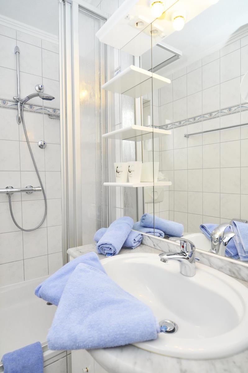 Badezimmer mit Dusche, Waschbecken und blauen Handtüchern.