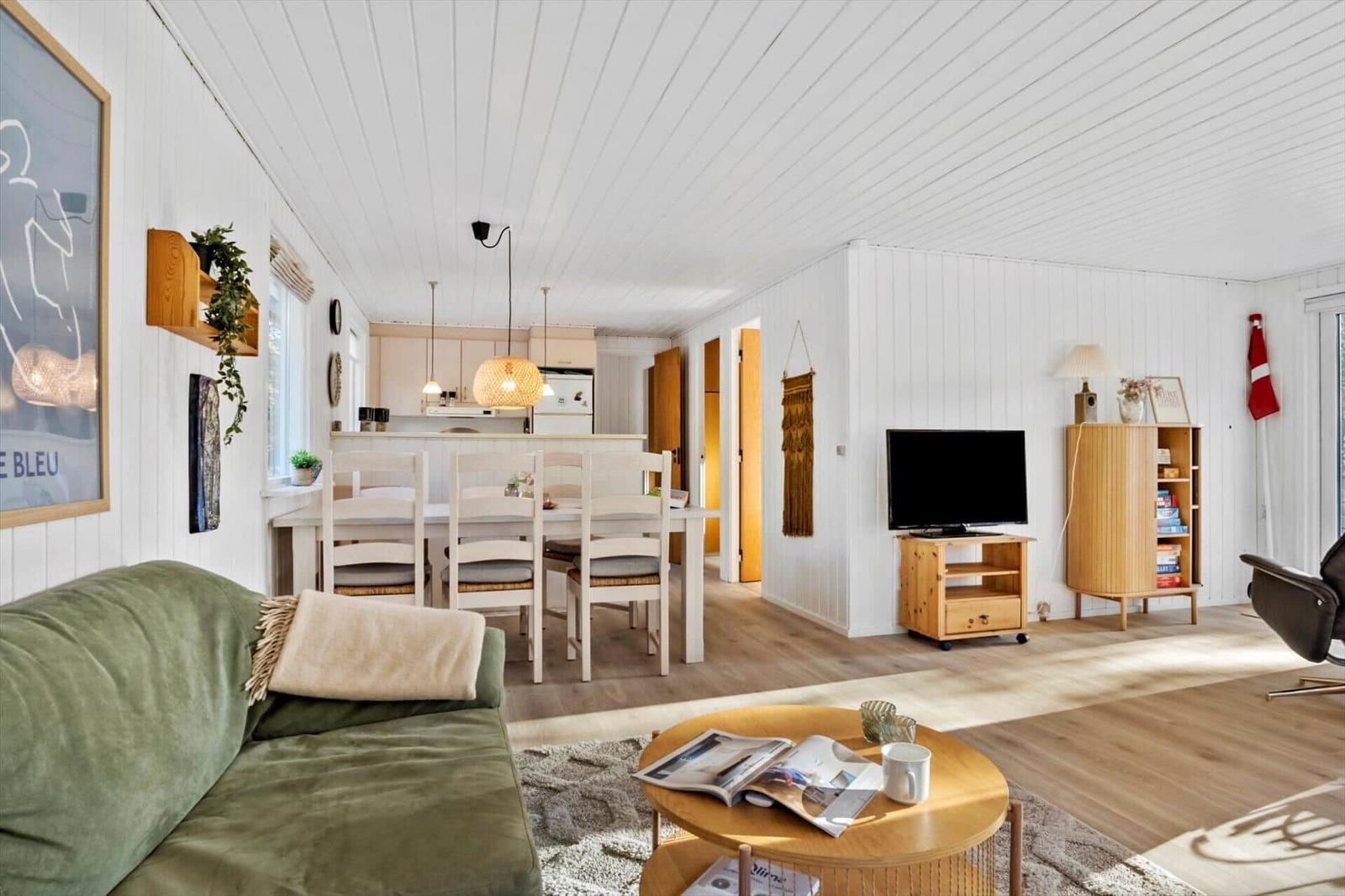 Wohnzimmer mit Sofa, Esstisch und Küche im Hintergrund.