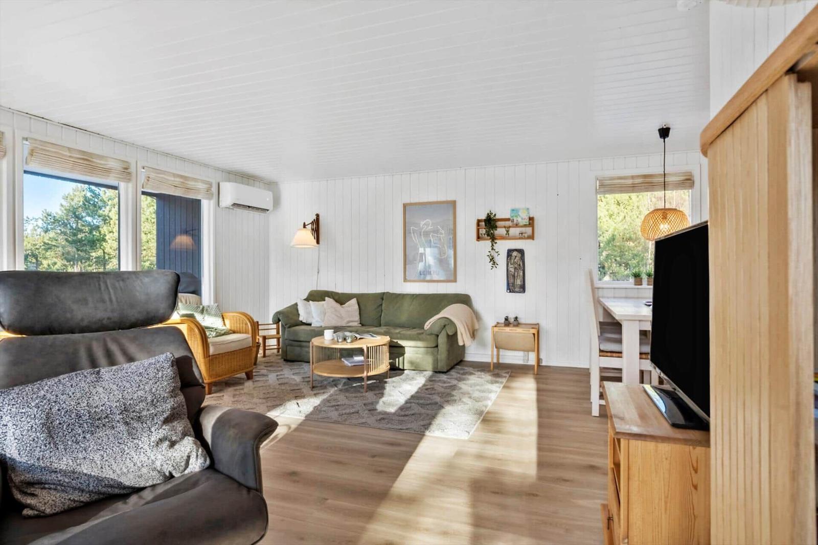 Wohnzimmer mit Sofa, Sessel und Esstisch. Holzboden und weiße Wände.