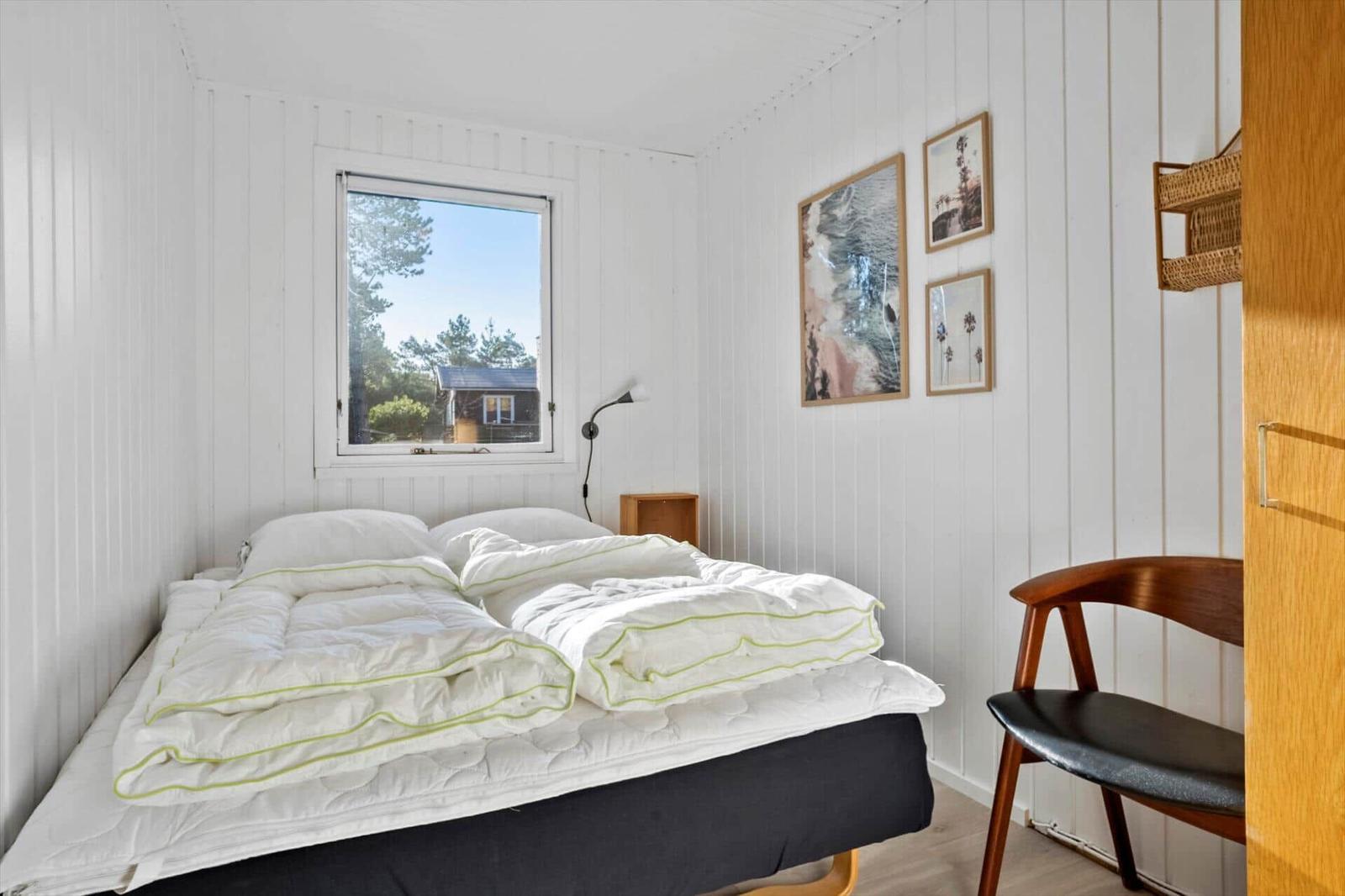 Schlafzimmer mit Bett, Stuhl und Fensterblick auf Wald.