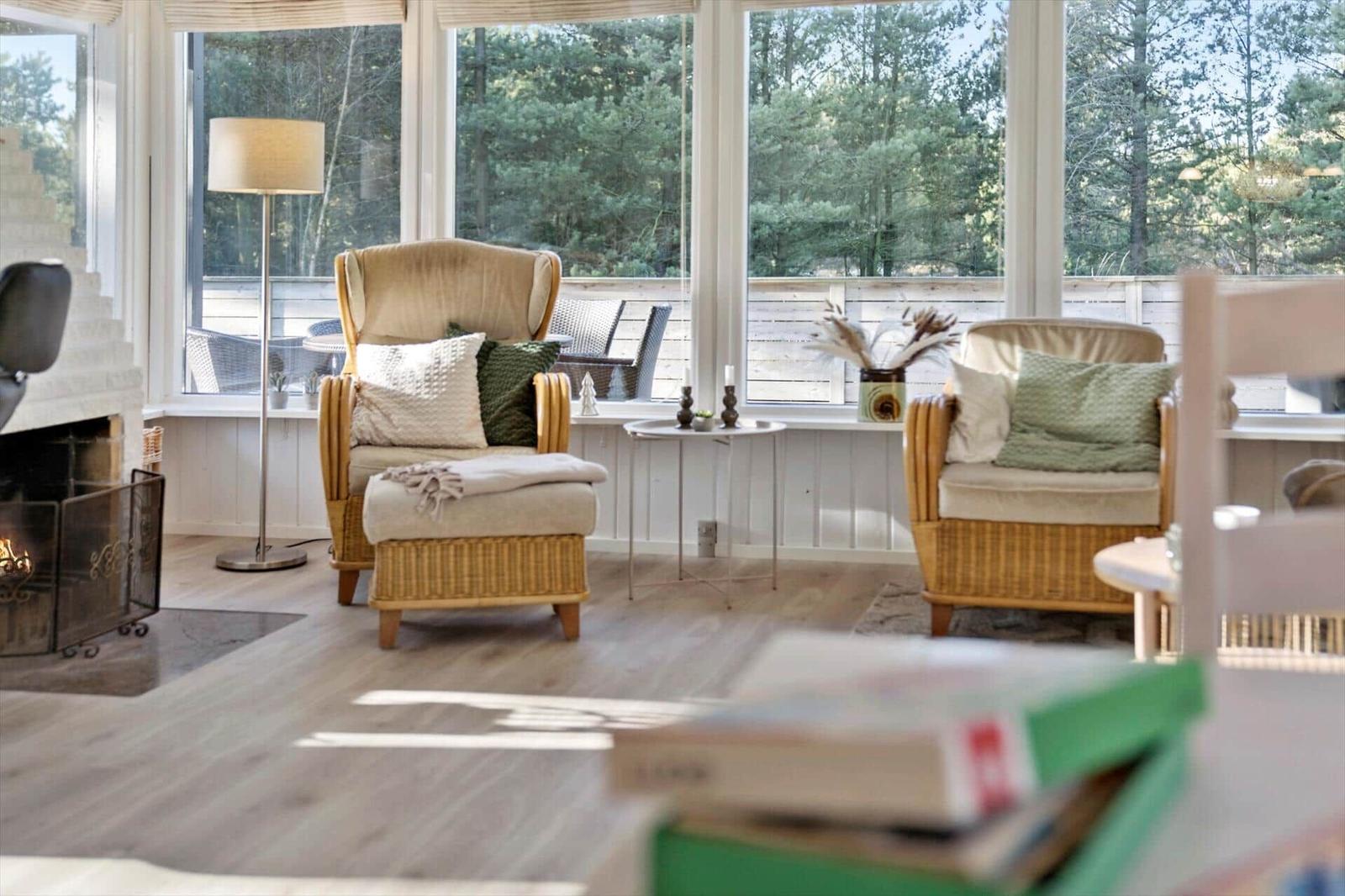 Wohnzimmer mit zwei Sesseln, Kamin und Blick auf Wald.