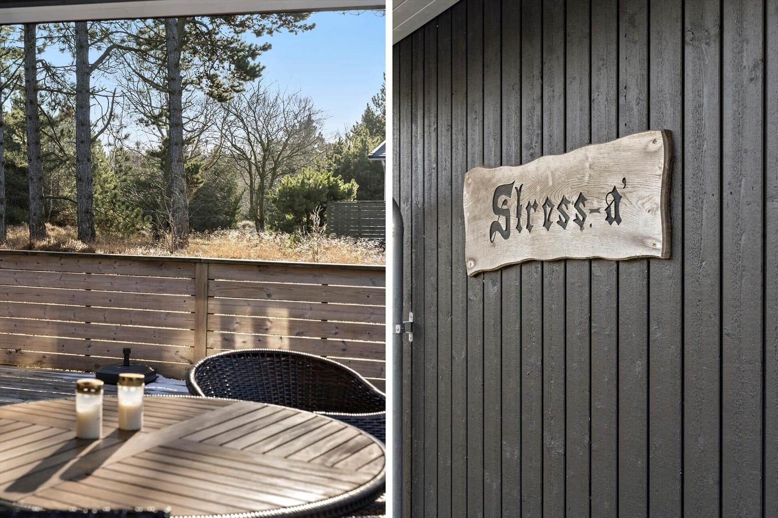 Terrasse mit Tisch und Stühlen. Holzschild mit Schriftzug an Wand.