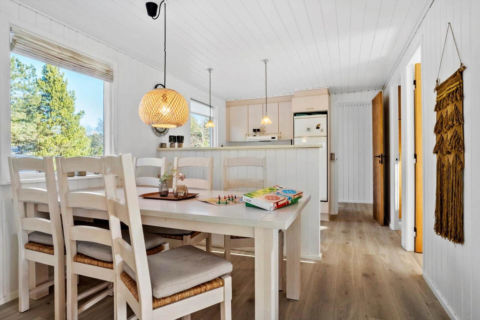 Essbereich mit Tisch, Stühlen und Blick auf Wald. Küche mit Kühlschrank und Holzboden.