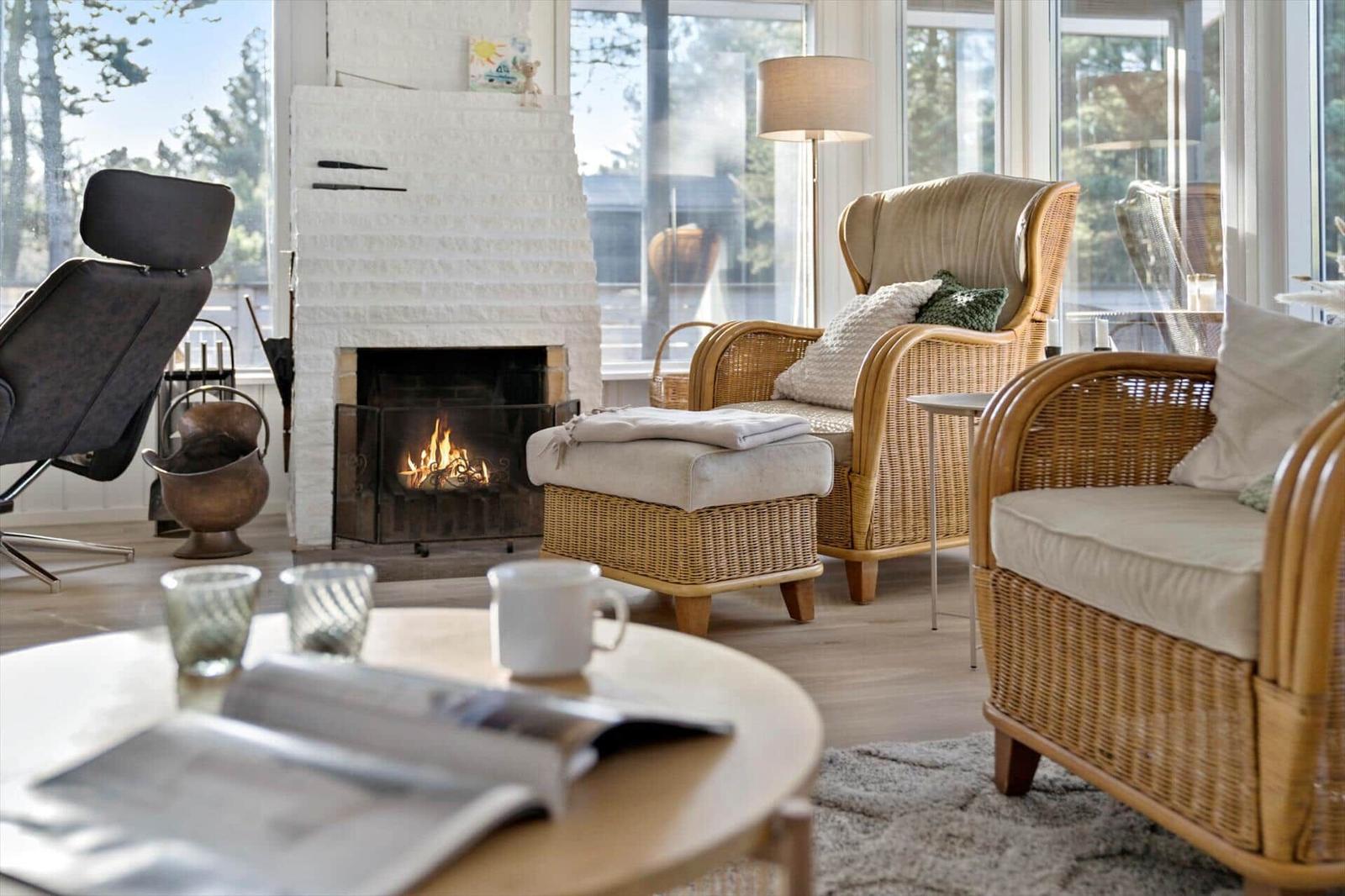 Wohnzimmer mit Kamin, Rattanmöbeln und großem Fensterblick.