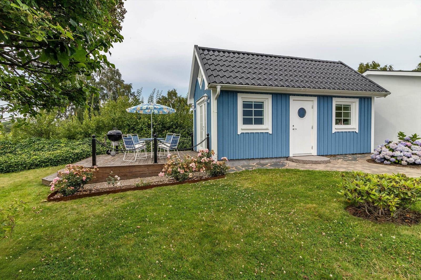 Blauer Holzhaus mit Terrasse, Grill und Garten.