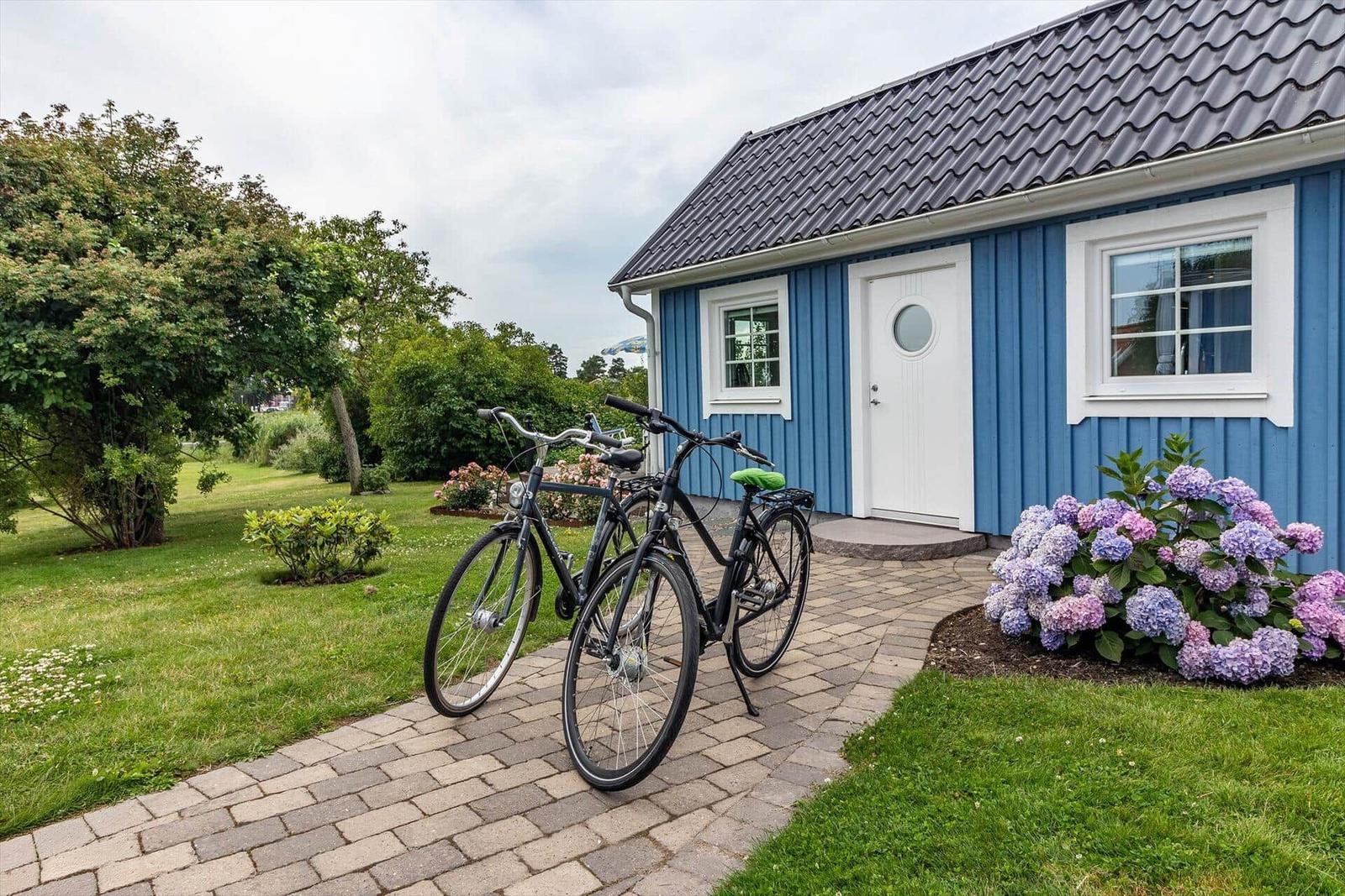 Blau gestrichenes Haus mit weißer Tür und Fenstern. Zwei Fahrräder stehen auf dem Kiesweg.